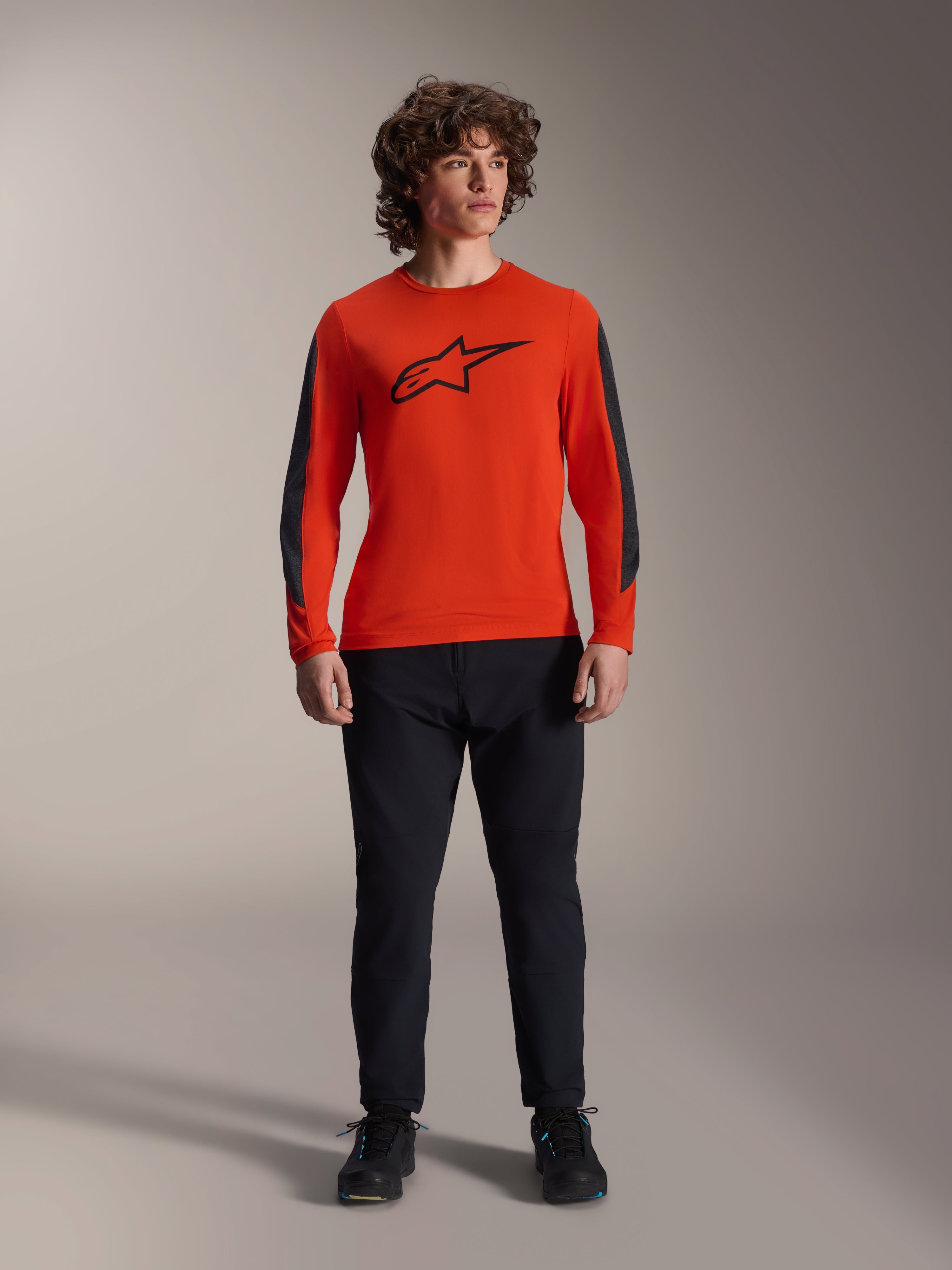 Alpinestars A-Dura Insert Astar Jersey - Long Sleeve, pomarańczowa koszulka (Spicy Orange) z czarnym logo Astar i ciemnoszarymi panelami na rękawach, zestawiona z czarnymi spodniami i butami MTB, wytrzymała konstrukcja tekstylna do jazdy w terenie