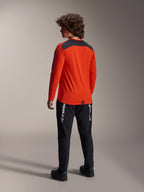 Widok z tyłu modelu ubranego w koszulkę Alpinestars A-Dura Insert Astar w kolorze Spicy Orange, koszulka MTB z długim rękawem z ciemnoszarym panelem na ramionach, zestawiona z czarnymi markowymi spodniami, odzież rowerowa off-road.