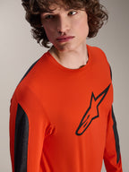 Alpinestars A-Dura Insert Astar Long Sleeve Jersey, koszulka MTB w kolorze Spicy Orange z dużym czarnym logo Astar na klatce piersiowej, ciemnoszare panele na rękawach, noszona przez modela w zbliżeniu studyjnym, teksturowana tkanina techniczna.