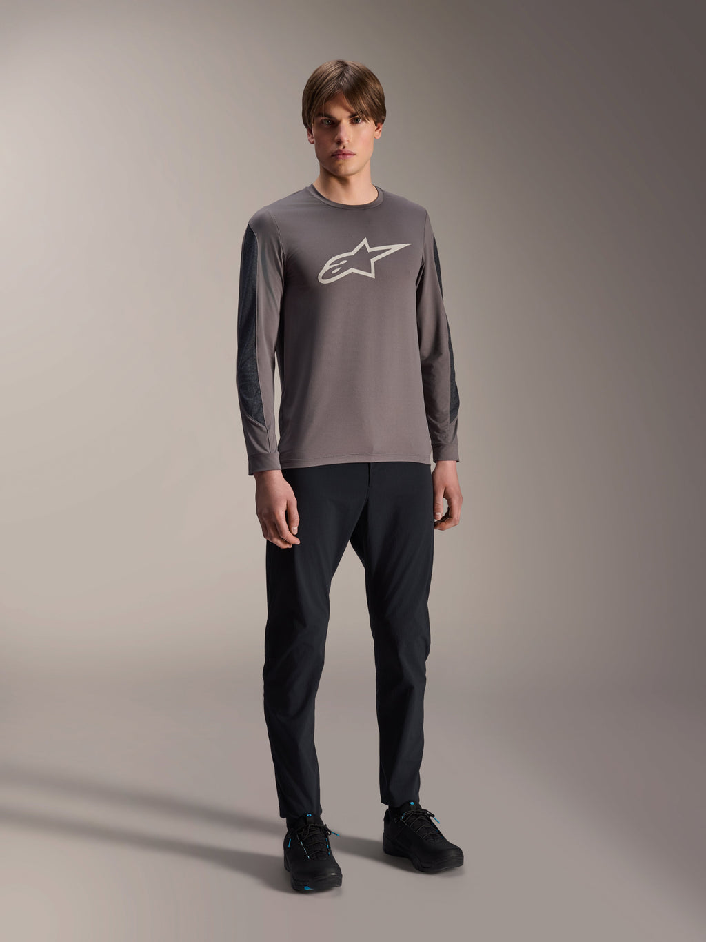 Alpinestars A-Dura Insert Astar Jersey, koszulka MTB z długim rękawem, ciemnoszara, z dużym białym logo na klatce piersiowej, zestawiona z czarnymi spodniami technicznymi i czarnymi butami, odzież do jazdy terenowej