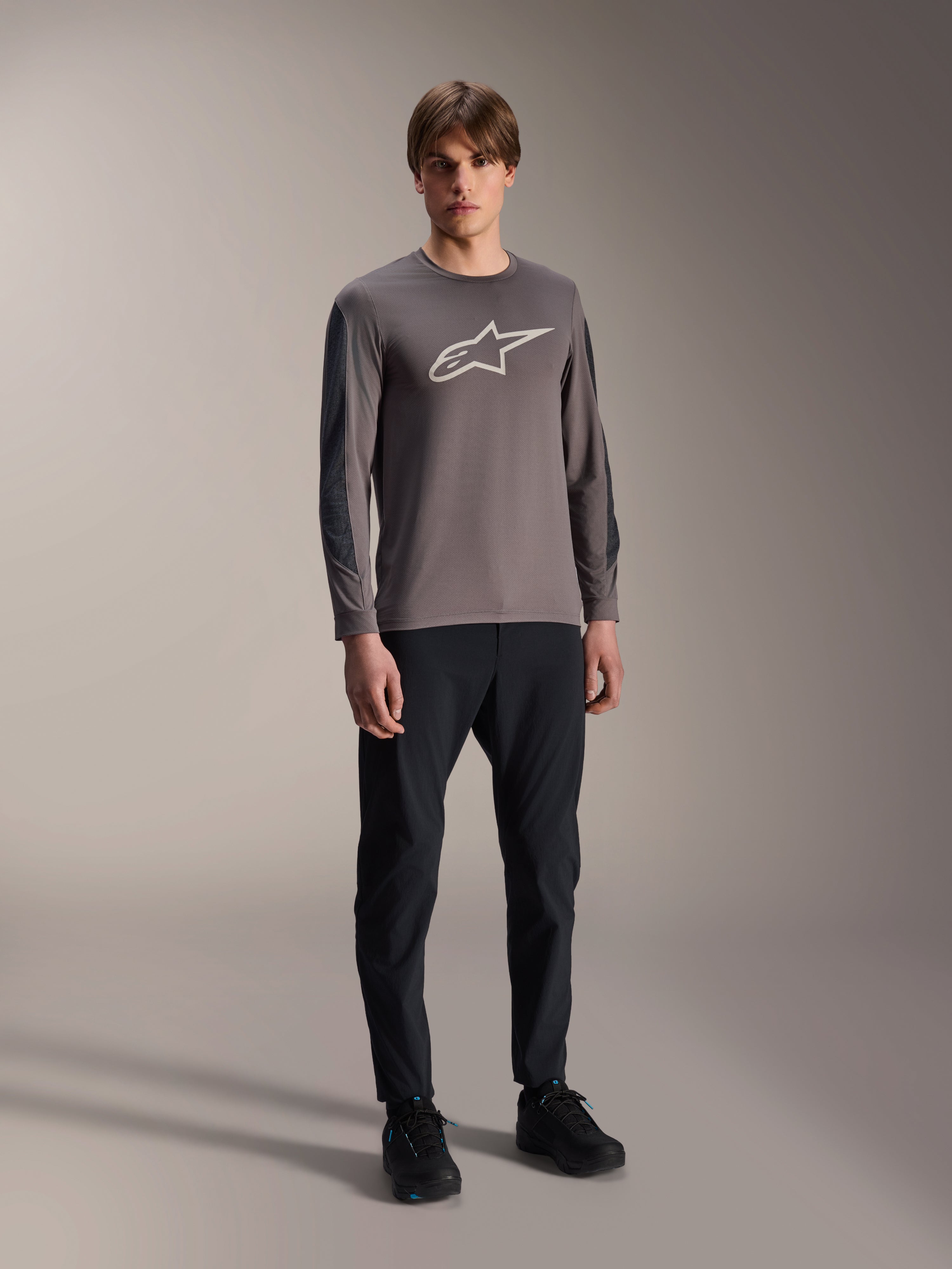 Alpinestars A-Dura Insert Astar Jersey, koszulka MTB z długim rękawem, ciemnoszara, z dużym białym logo na klatce piersiowej, zestawiona z czarnymi spodniami technicznymi i czarnymi butami, odzież do jazdy terenowej