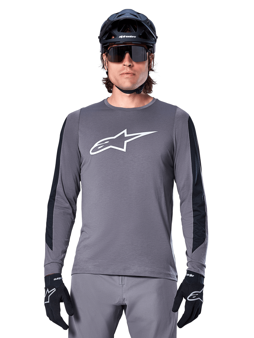 Koszulka z długim rękawem Alpinestars A-Dura Dri Astar, ciemnoszara, z dużym białym logo Astar na piersi i czarnymi siatkowymi panelami na rękawach, noszona przez rowerzystę w czarnym kasku MTB i okularach sportowych, odzież rowerowa MTB