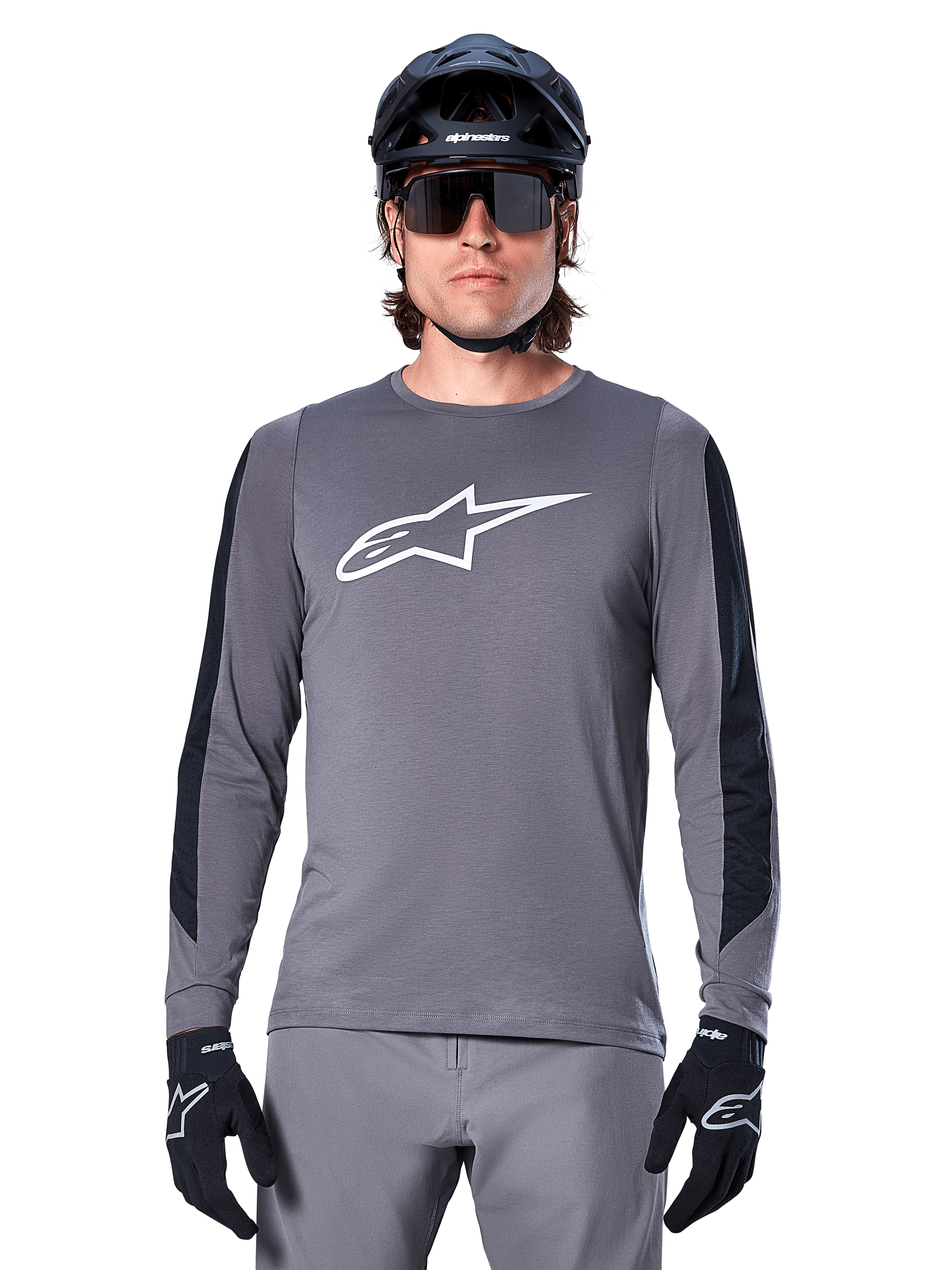 Koszulka z długim rękawem Alpinestars A-Dura Dri Astar, ciemnoszara, z dużym białym logo Astar na piersi i czarnymi siatkowymi panelami na rękawach, noszona przez rowerzystę w czarnym kasku MTB i okularach sportowych, odzież rowerowa MTB