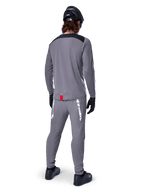 Alpinestars A-Dura Dri Astar Jersey - Long Sleeve, ciemnoszara, widok od tyłu na rowerzystę w pasujących spodniach i czarnym kasku, posiada czarne panele na ramionach i małą czerwoną metkę u dołu, techniczna odzież do jazdy terenowej