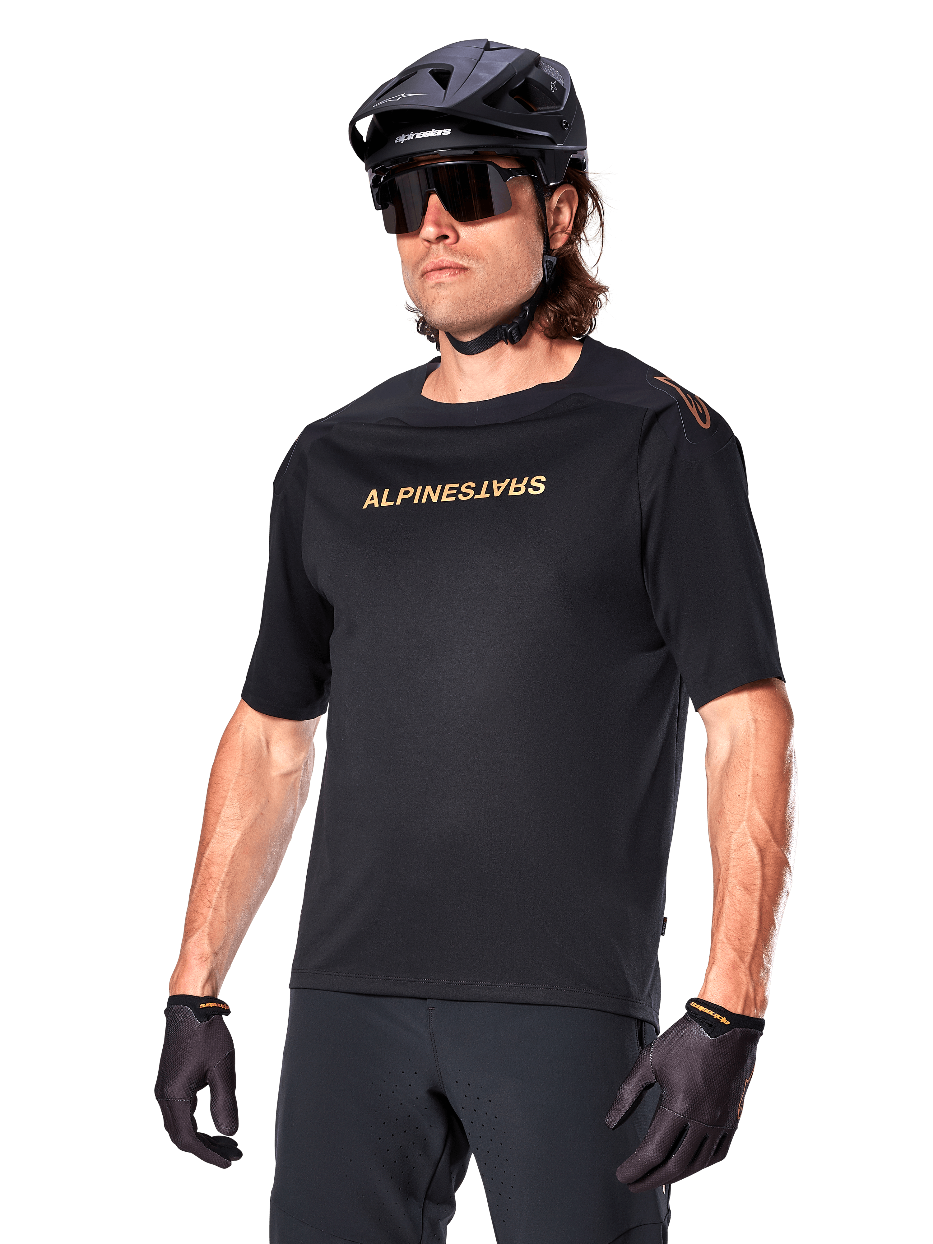 Alpinestars A-Aria Polartec Switch Jersey z krótkim rękawem, czarna koszulka rowerowa ze złotym brandingiem Alpinestars, czarny kask, okulary przeciwsłoneczne i rękawice, techniczna odzież MTB