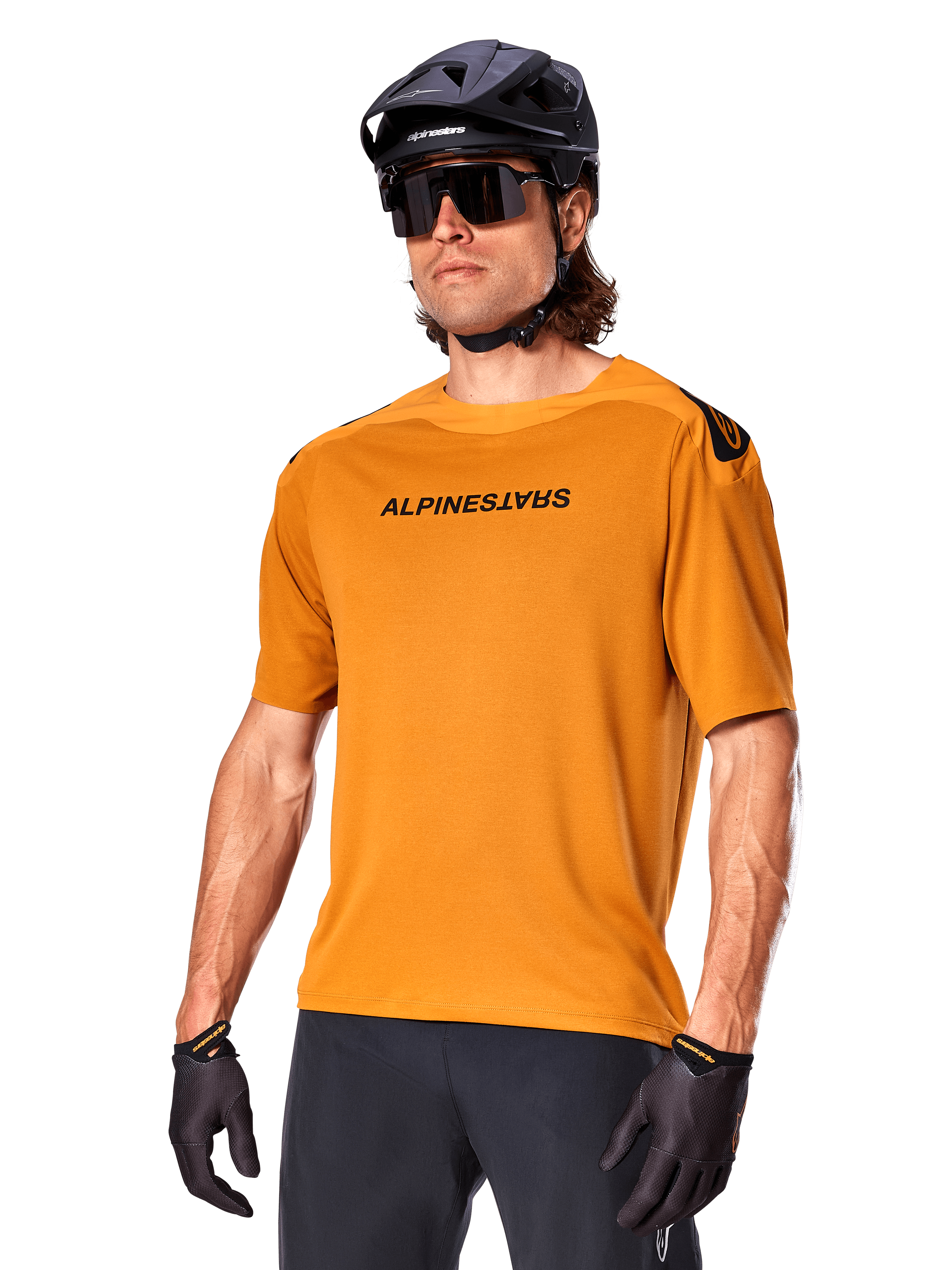 Alpinestars A-Aria Polartec Switch Jersey, koszulka MTB z krótkim rękawem, w kolorze ciemnego złota z czarnym brandingiem, noszona przez modela w czarnym kasku, okularach przeciwsłonecznych i rękawiczkach rowerowych, wysokiej jakości odzież do kolarstwa górskiego