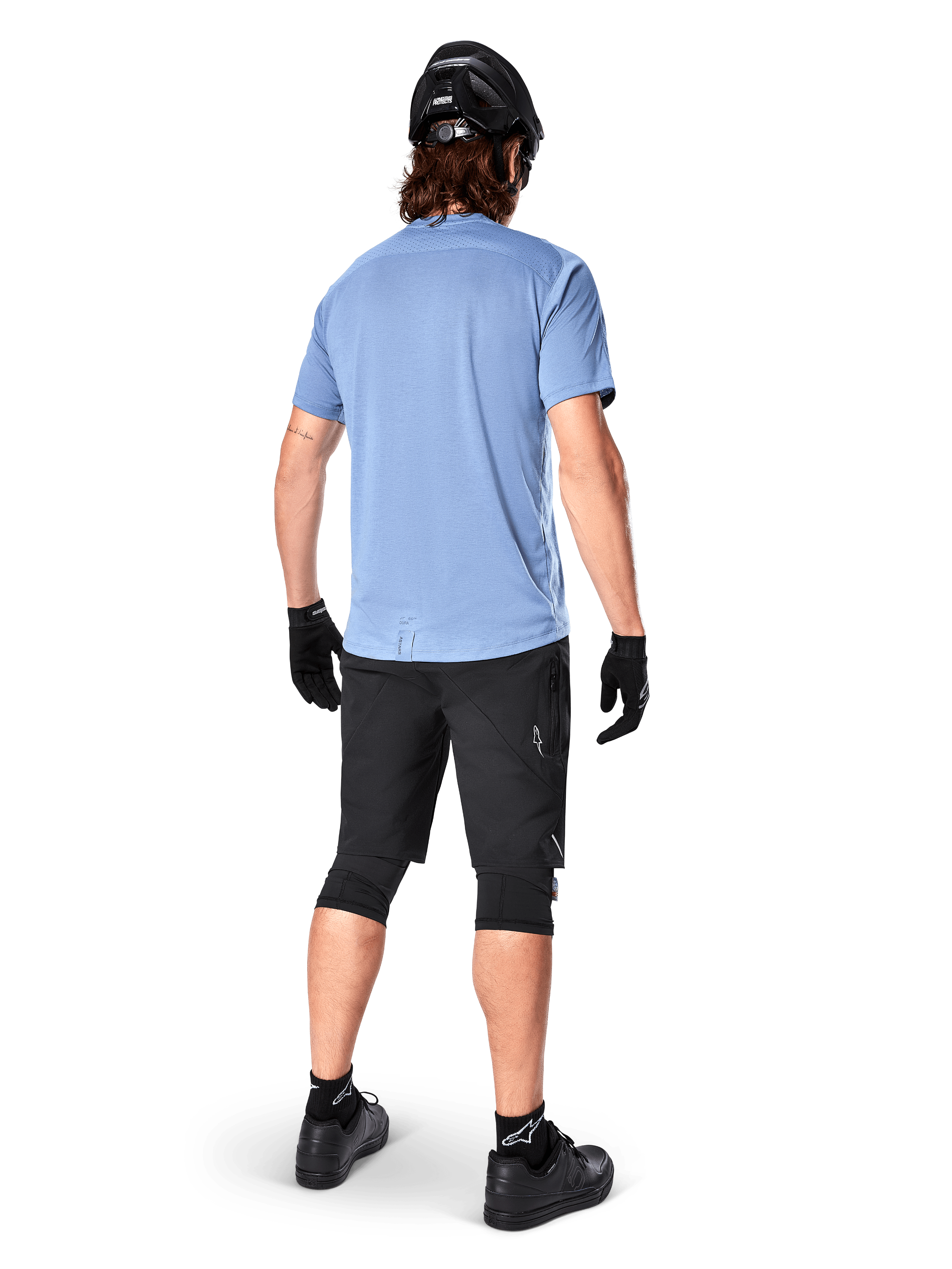 Koszulka z krótkim rękawem Alpinestars A-Dura Dri Astar, kolor Infinity Blue, widok z tyłu, zestawiona z czarnymi szortami rowerowymi i kaskiem, techniczna odzież rowerowa z materiału odprowadzającego wilgoć, przedłużony tył