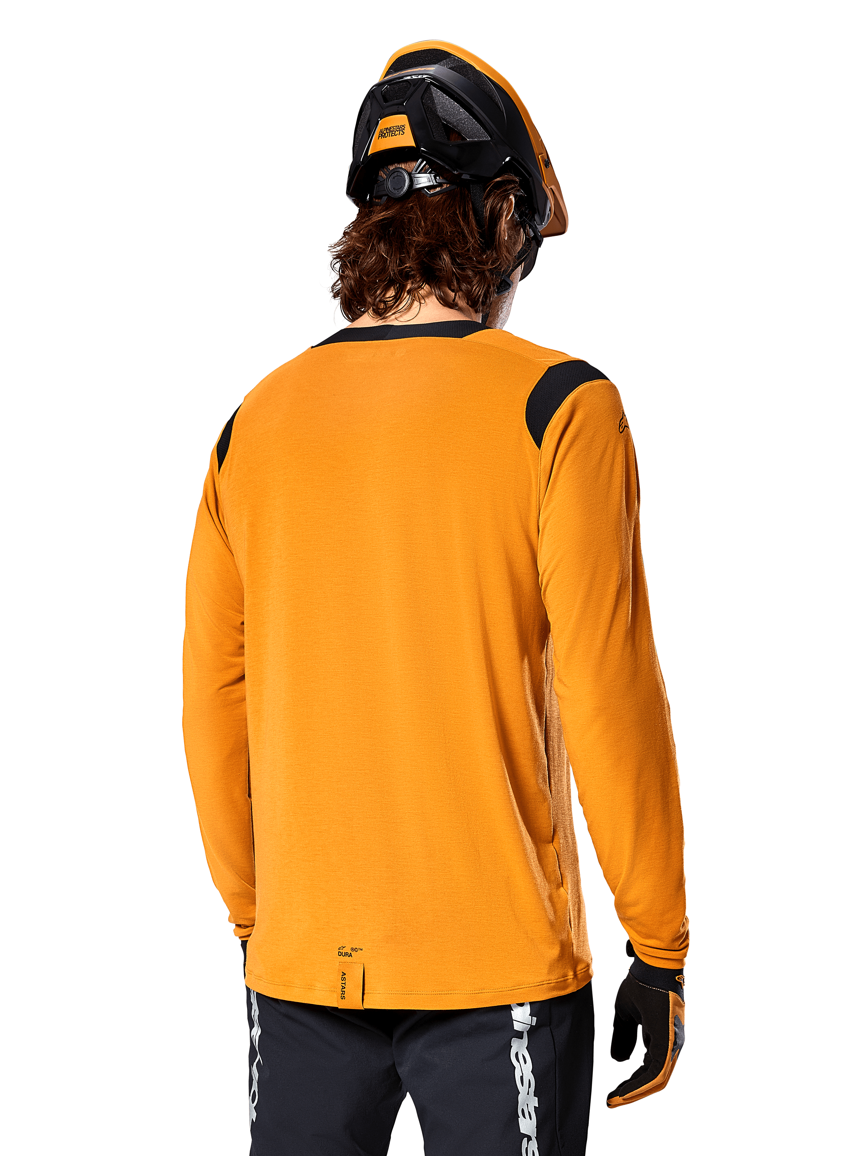 Alpinestars A-Dura Dri Wool Long Sleeve Jersey w kolorze Dark Gold, widok z tyłu na rowerzystę w kasku MTB i rękawiczkach, czarne panele z siatki na ramionach i przedłużony tył, techniczna odzież rowerowa do jazdy po szlakach