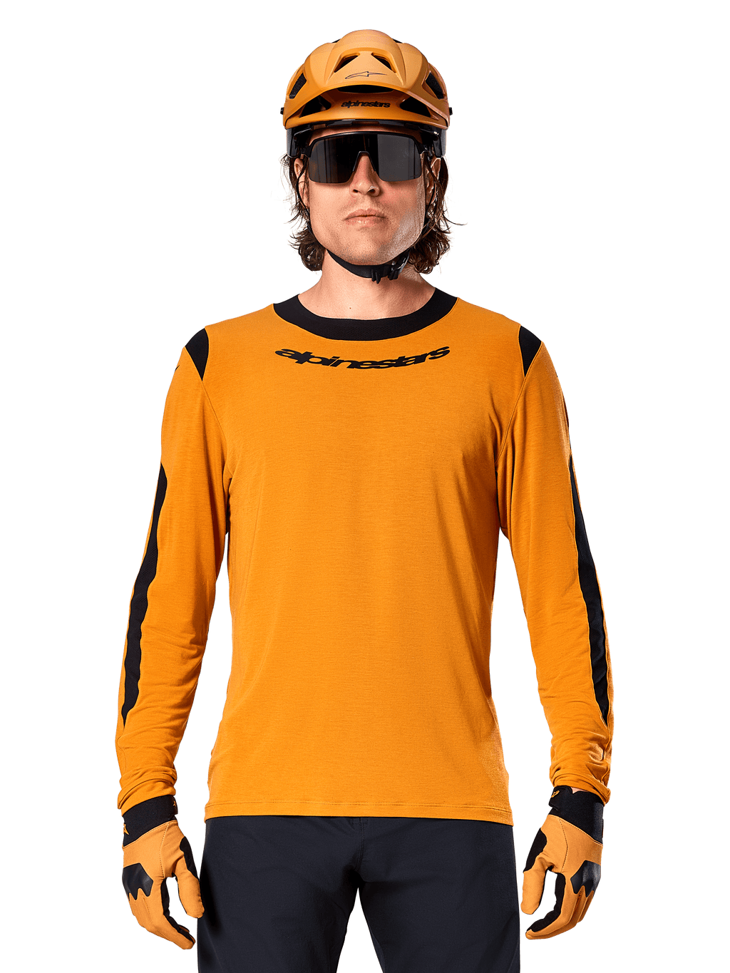Męski model w koszulce z długim rękawem Alpinestars A-Dura Dri Wool w kolorze Dark Gold, dopasowany złoty kask MTB i rękawice, czarne panele z siatki na ramionach i rękawach, czarny napis Alpinestars na piersi, ciemne okulary przeciwsłoneczne i spodnie, techniczna odzież do kolarstwa górskiego