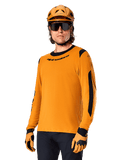 Alpinestars A-Dura Dri Wool Jersey z długim rękawem, koszulka rowerowa MTB, ciemnozłota i czarna, z odprowadzającej wilgoć mieszanki wełny merino i paneli siatkowych, rowerzysta w pasującym kasku, okularach przeciwsłonecznych i rękawicach