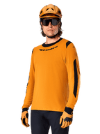 Alpinestars A-Dura Dri Wool Jersey z długim rękawem, koszulka rowerowa MTB, ciemnozłota i czarna, z odprowadzającej wilgoć mieszanki wełny merino i paneli siatkowych, rowerzysta w pasującym kasku, okularach przeciwsłonecznych i rękawicach
