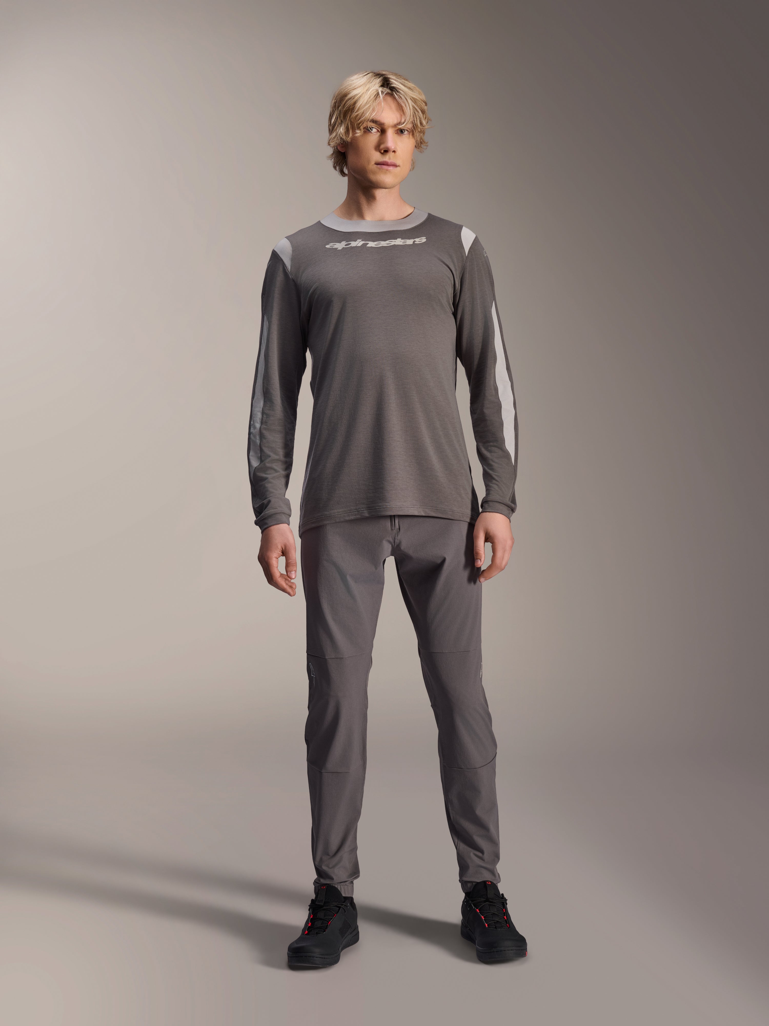 Alpinestars A-Dura Dri Wool Long Sleeve Jersey, ciemnoszara, model w pasujących szarych spodniach i czarnych butach, białe logo Alpinestars na piersi, jasnoszare panele z siatki na ramionach i rękawach, techniczna odzież na rower górski