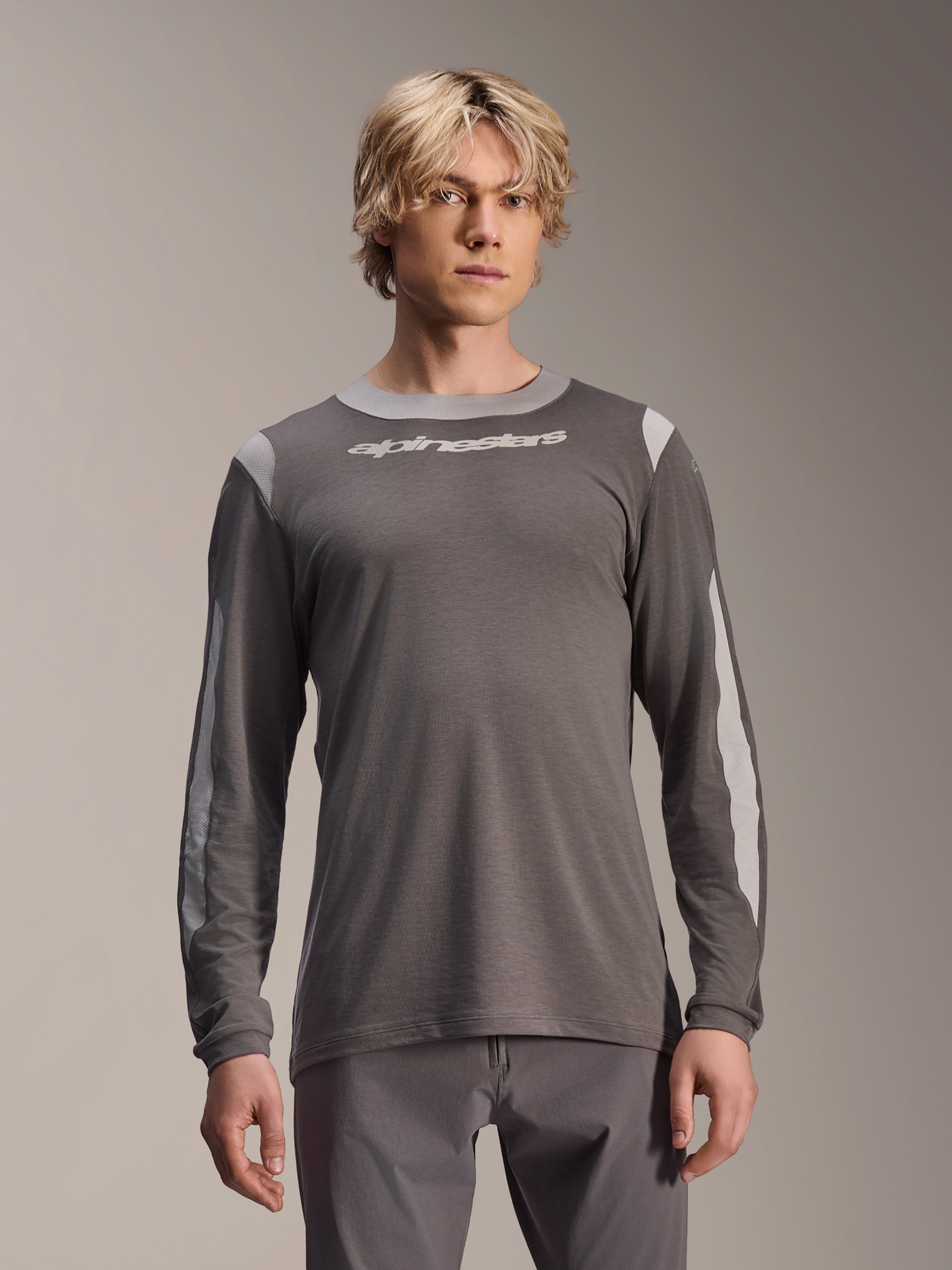 Alpinestars A-Dura Dri Wool Jersey Long Sleeve, ciemnoszara koszulka z długim rękawem noszona przez modela, jasnoszare panele z siateczki na ramionach i rękawach, białe logo na piersi, profesjonalna odzież rowerowa MTB
