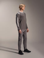 Męski model w koszulce Alpinestars A-Dura Dri Wool z długim rękawem w kolorze ciemnoszarym, zestawionej z pasującymi szarymi spodniami i czarnymi butami, jasnoszare panele z siateczki na ramionach i rękawach, techniczna odzież MTB do jazdy terenowej