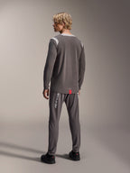 Męski model w koszulce Alpinestars A-Dura Dri Wool Long Sleeve, ciemnoszara z jasnoszarymi siateczkowymi panelami na ramionach, dopasowane ciemnoszare spodnie rowerowe, widok z tyłu prezentujący przedłużony tył, odzież MTB