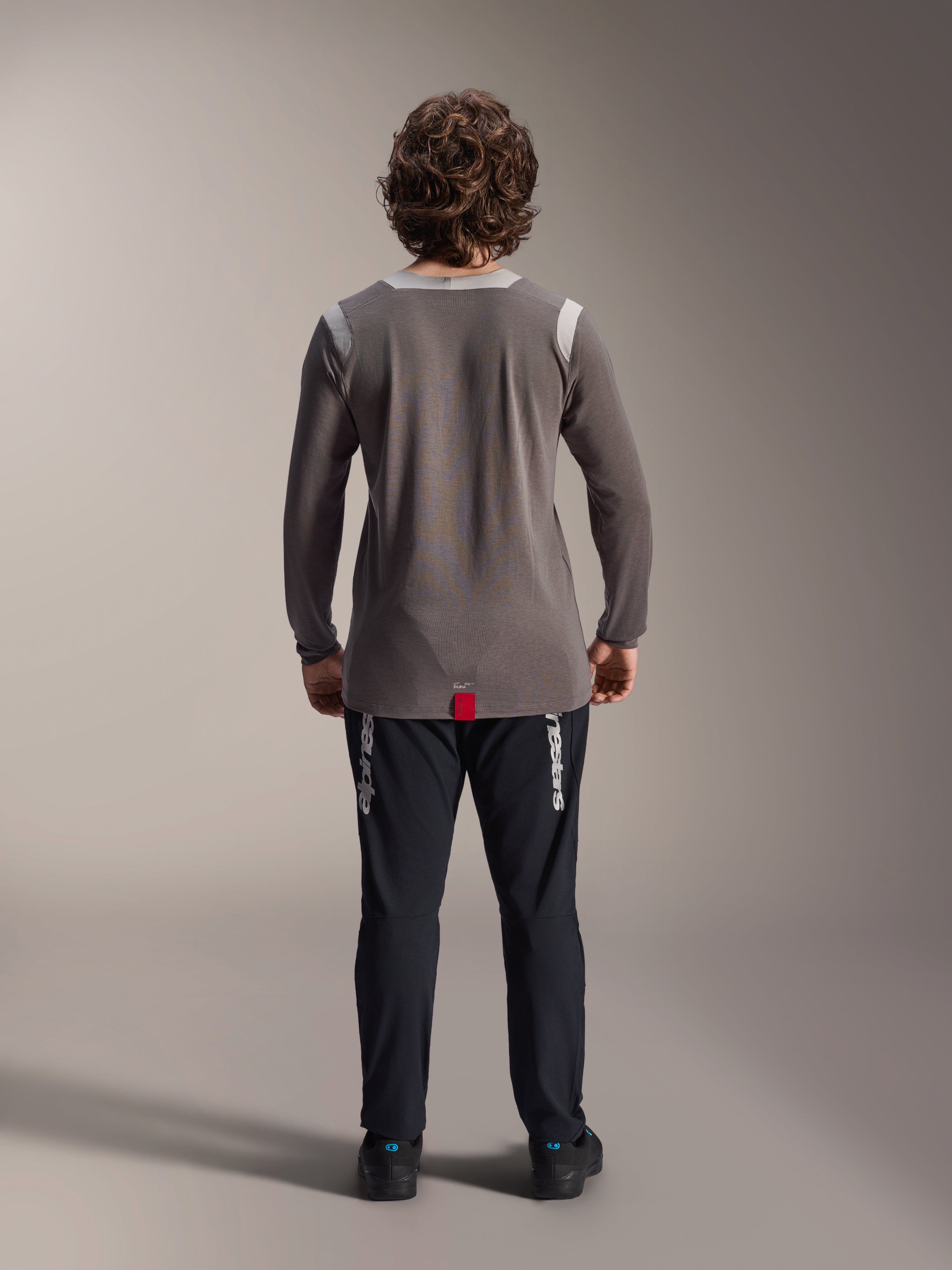 Spodnie Alpinestars A-Dura Elite i koszulka z długim rękawem A-Dura Dri Wool, czarne spodnie z białym brandingiem, szara koszulka techniczna, widok z tyłu stroju na rower górski, wytrzymała odzież rowerowa terenowa