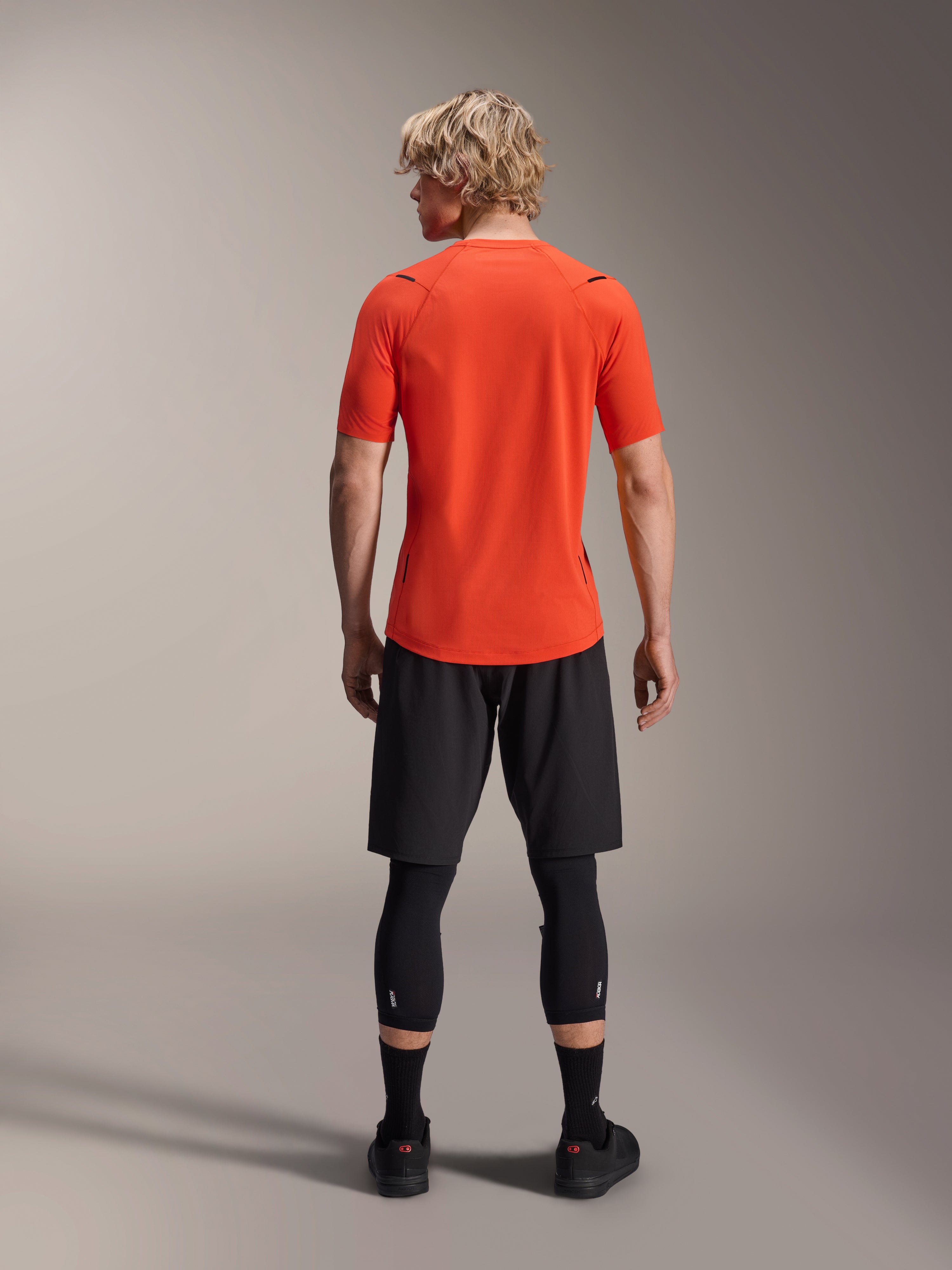 Alpinestars A-Aria Astar Jersey, koszulka MTB z krótkim rękawem, kolor Spicy Orange, widok z tyłu prezentujący sportowy krój i przedłużony tył, zestawiona z czarnymi szortami rowerowymi i legginsami