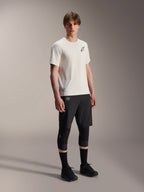 Alpinestars A-Aria Astar Jersey, koszulka z krótkim rękawem, kolor ecru, czarne logo na piersi, noszona z czarnymi szortami rowerowymi i ochraniaczami na kolana, lekka odzież wyczynowa MTB