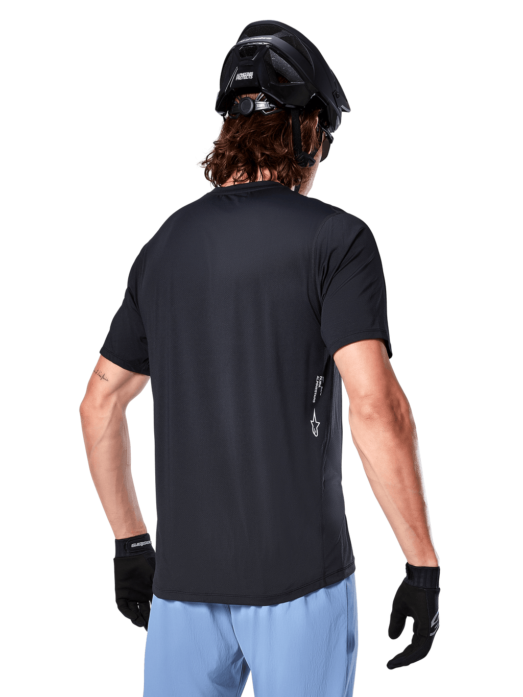 Alpinestars A-Dura Oscar Jersey, koszulka rowerowa z krótkim rękawem, czarna, widok z tyłu na kolarza, w zestawieniu z jasnoniebieskimi szortami i czarnym kaskiem MTB, małe białe logo z boku, odzież wyczynowa do kolarstwa górskiego