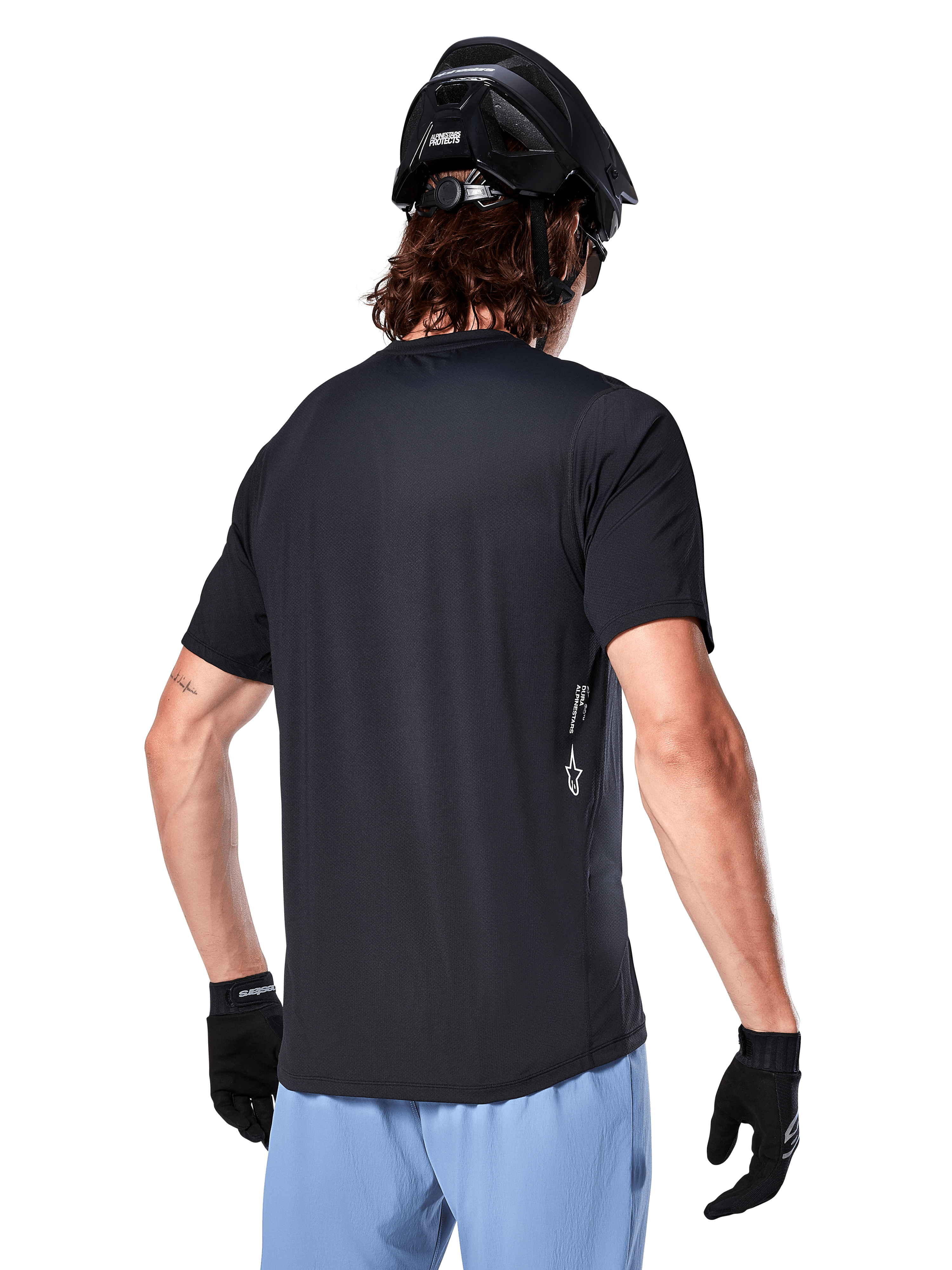 Alpinestars A-Dura Oscar Jersey, koszulka rowerowa z krótkim rękawem, czarna, widok z tyłu na kolarza, w zestawieniu z jasnoniebieskimi szortami i czarnym kaskiem MTB, małe białe logo z boku, odzież wyczynowa do kolarstwa górskiego