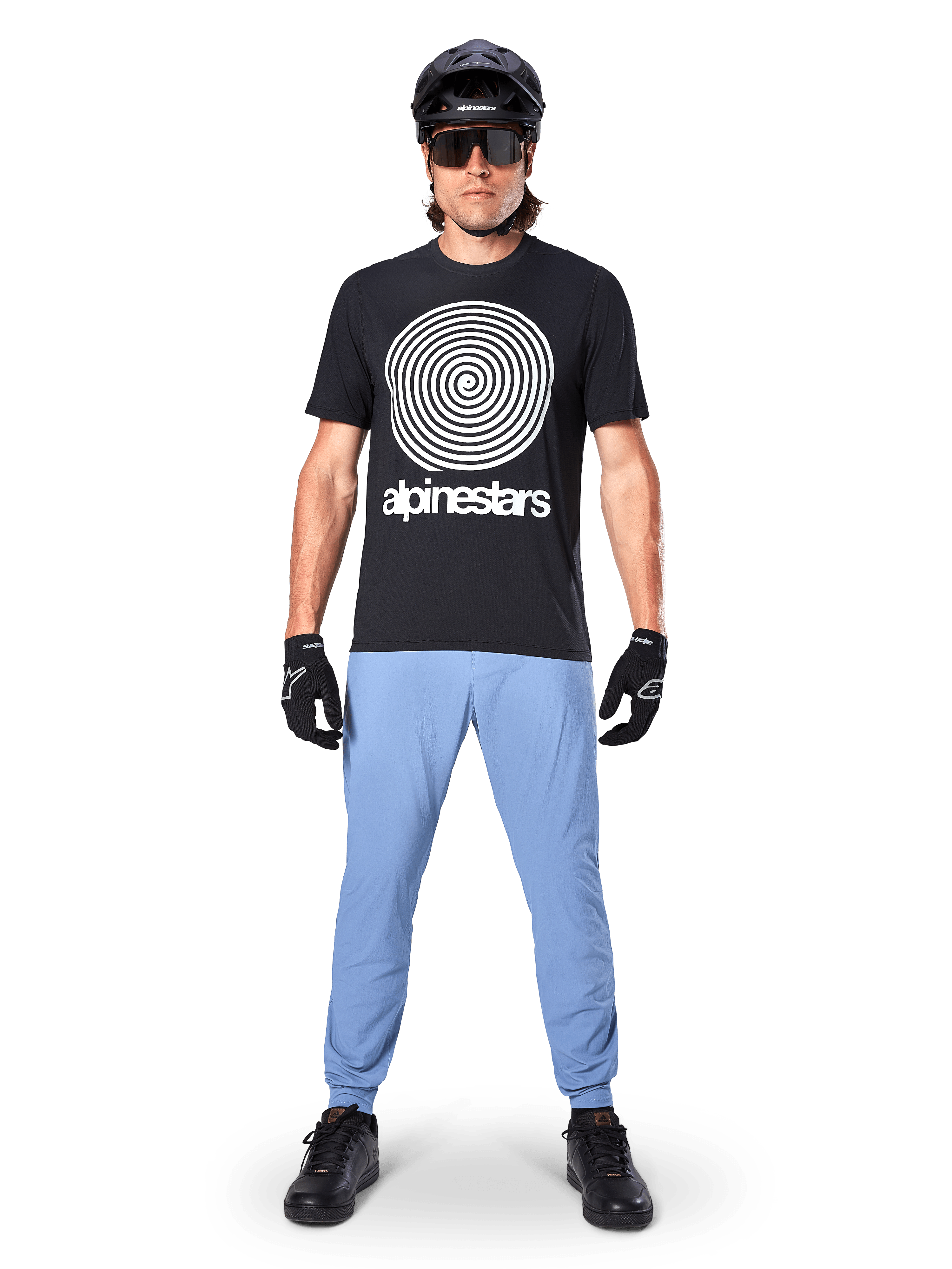 Alpinestars A-Dura Oscar Jersey - krótki rękaw, czarna koszulka MTB, z dużą białą grafiką spiralną Oscar w stylu vintage i napisem marki, noszona z jasnoniebieskimi spodniami, czarnym kaskiem, okularami przeciwsłonecznymi i czarnymi rękawiczkami, wydajna odzież do kolarstwa górskiego