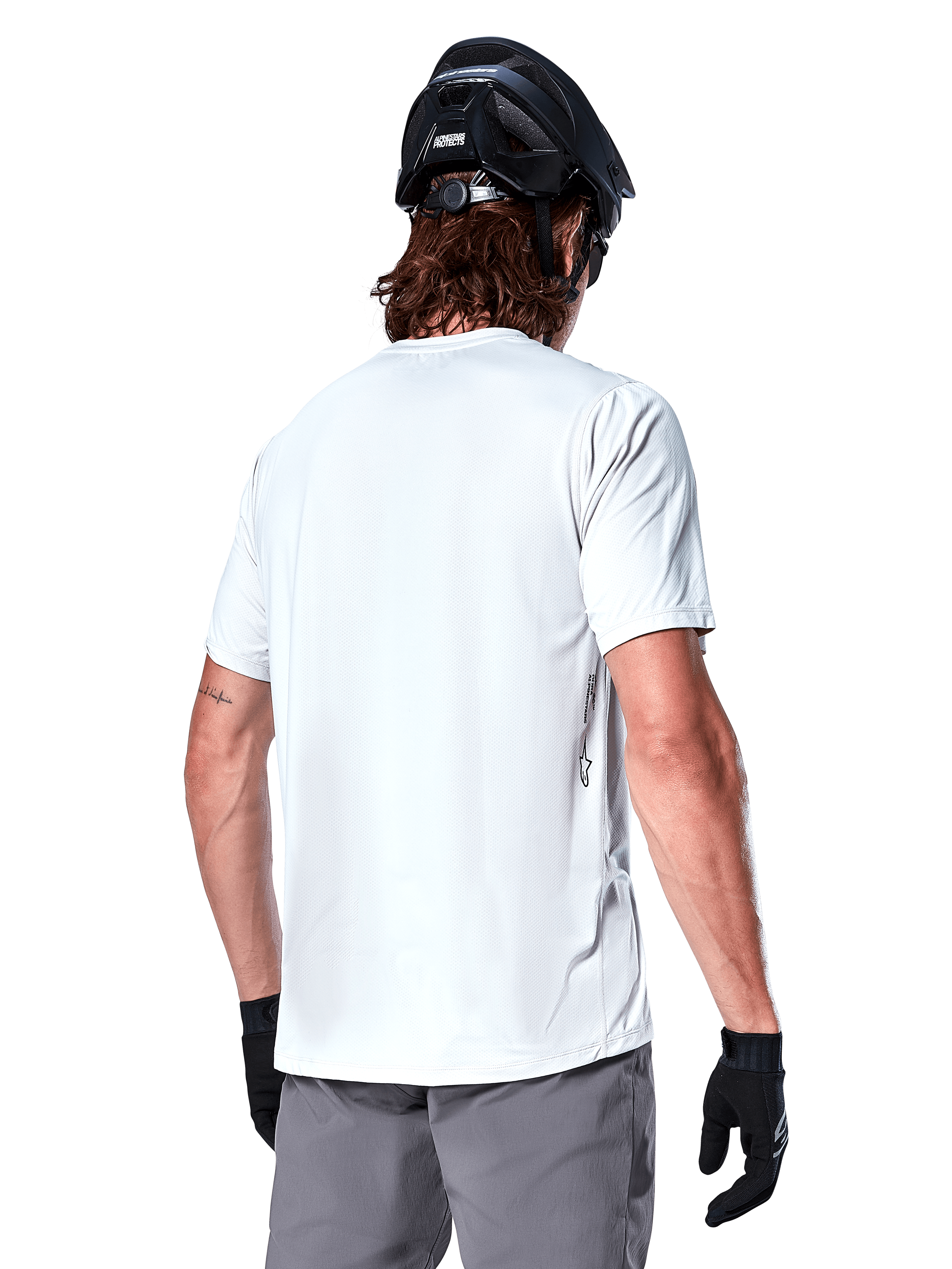 Alpinestars A-Dura Oscar Jersey, koszulka MTB z krótkim rękawem, biała (White Dove), widok od tyłu na rowerzystę w czarnym kasku, szarych szortach i czarnych rękawiczkach, techniczna odzież rowerowa