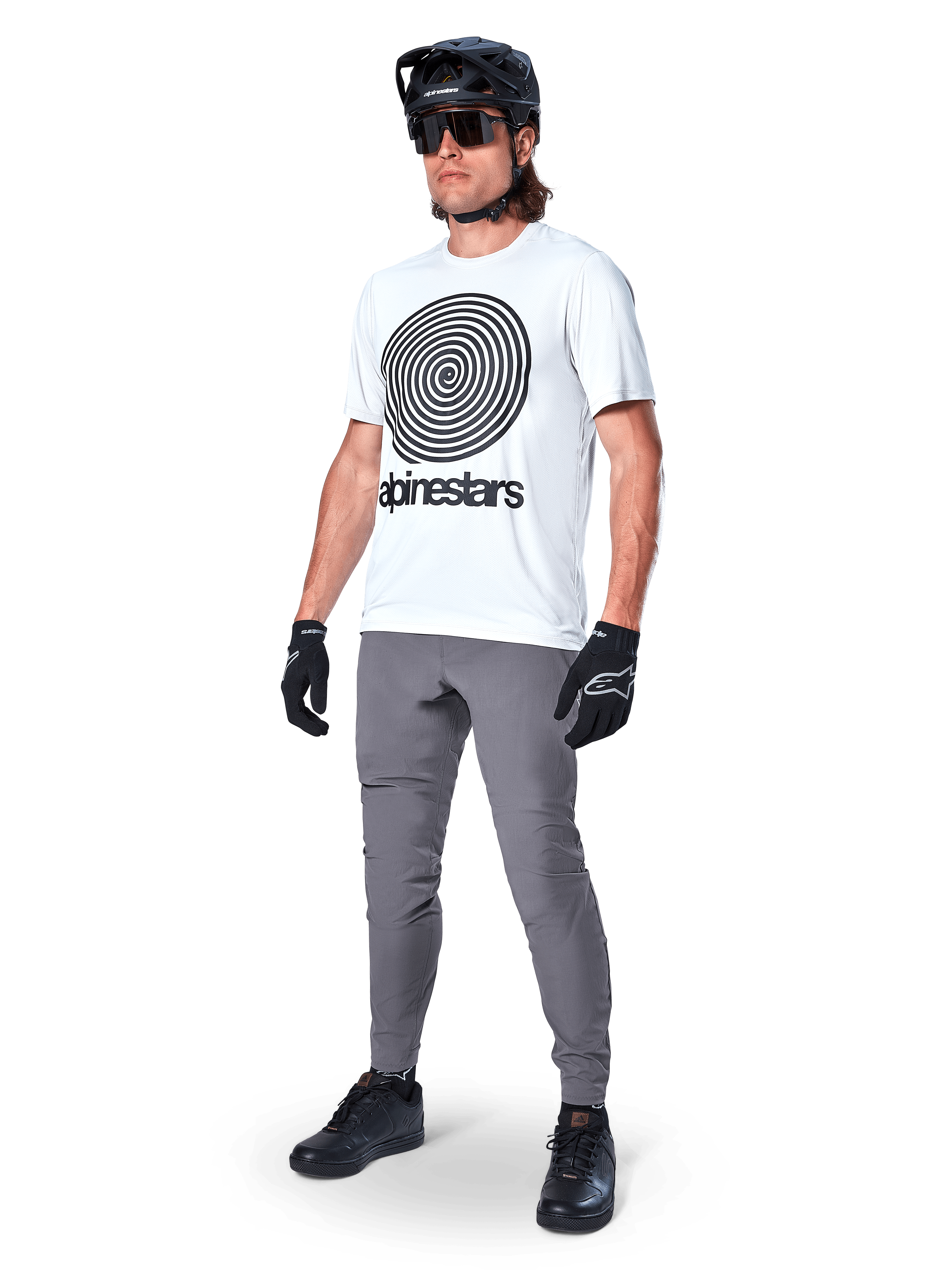 Koszulka Alpinestars A-Dura Oscar z krótkim rękawem, kolor White Dove z dużą czarną spiralną grafiką, noszona przez kolarza w szarych spodniach MTB, czarnym kasku i rękawiczkach, wydajna odzież rowerowa do jazdy w terenie