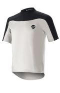Alpinestars Drop Meta Jersey z krótkim rękawem, koszulka do kolarstwa górskiego, jasnoszara i czarna, oddychająca konstrukcja z siateczki, czarny karczek na ramionach, okrągły dekolt i przedłużony tył dla lepszej osłony.