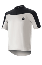 Alpinestars Drop Meta Jersey z krótkim rękawem, koszulka do kolarstwa górskiego, jasnoszara i czarna, oddychająca konstrukcja z siateczki, czarny karczek na ramionach, okrągły dekolt i przedłużony tył dla lepszej osłony.