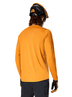 Alpinestars A-Dura Rocker Long Sleeve Jersey, ciemnozłoty, widok z tyłu na rowerzystę ubranego w czarno-pomarańczowy kask MTB, ciemne spodnie i dopasowane rękawiczki, swobodna odzież do kolarstwa górskiego