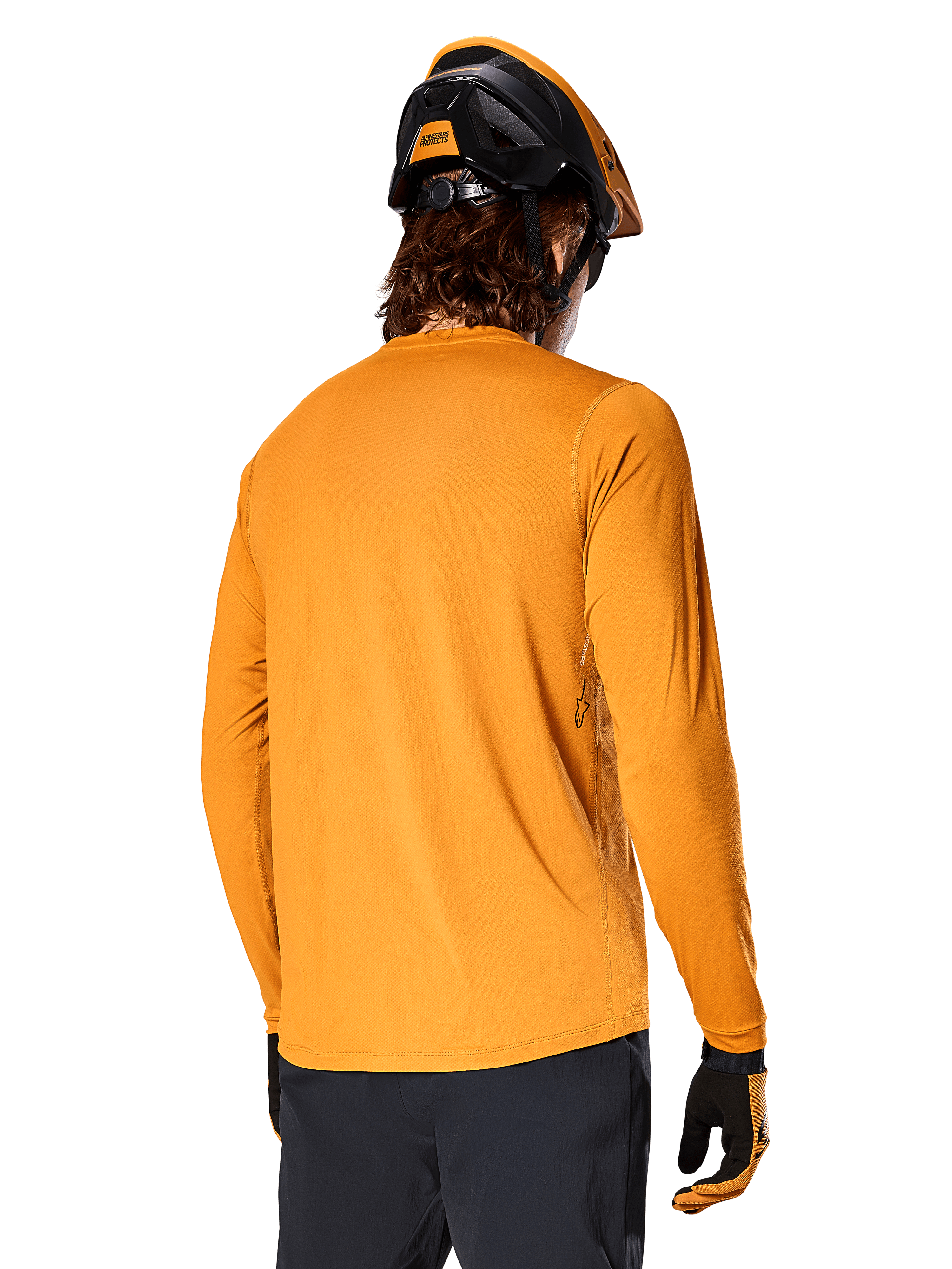 Alpinestars A-Dura Rocker Long Sleeve Jersey, ciemnozłoty, widok z tyłu na rowerzystę ubranego w czarno-pomarańczowy kask MTB, ciemne spodnie i dopasowane rękawiczki, swobodna odzież do kolarstwa górskiego
