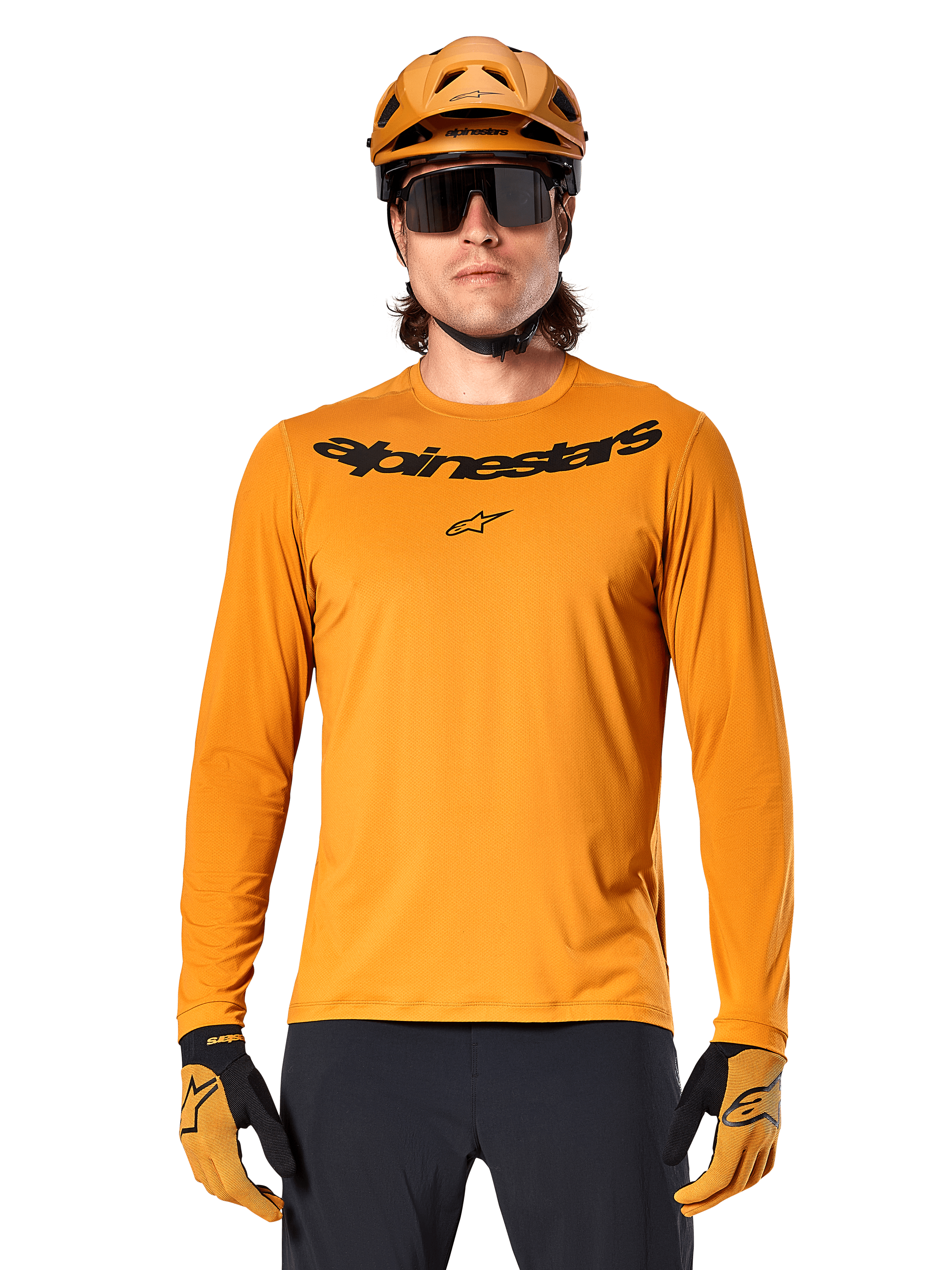 Koszulka z długim rękawem Alpinestars A-Dura Rocker w kolorze ciemnozłotym, z czarnym logotypem na piersi, noszona z pasującym złotym kaskiem i rękawicami do jazdy na rowerze górskim.