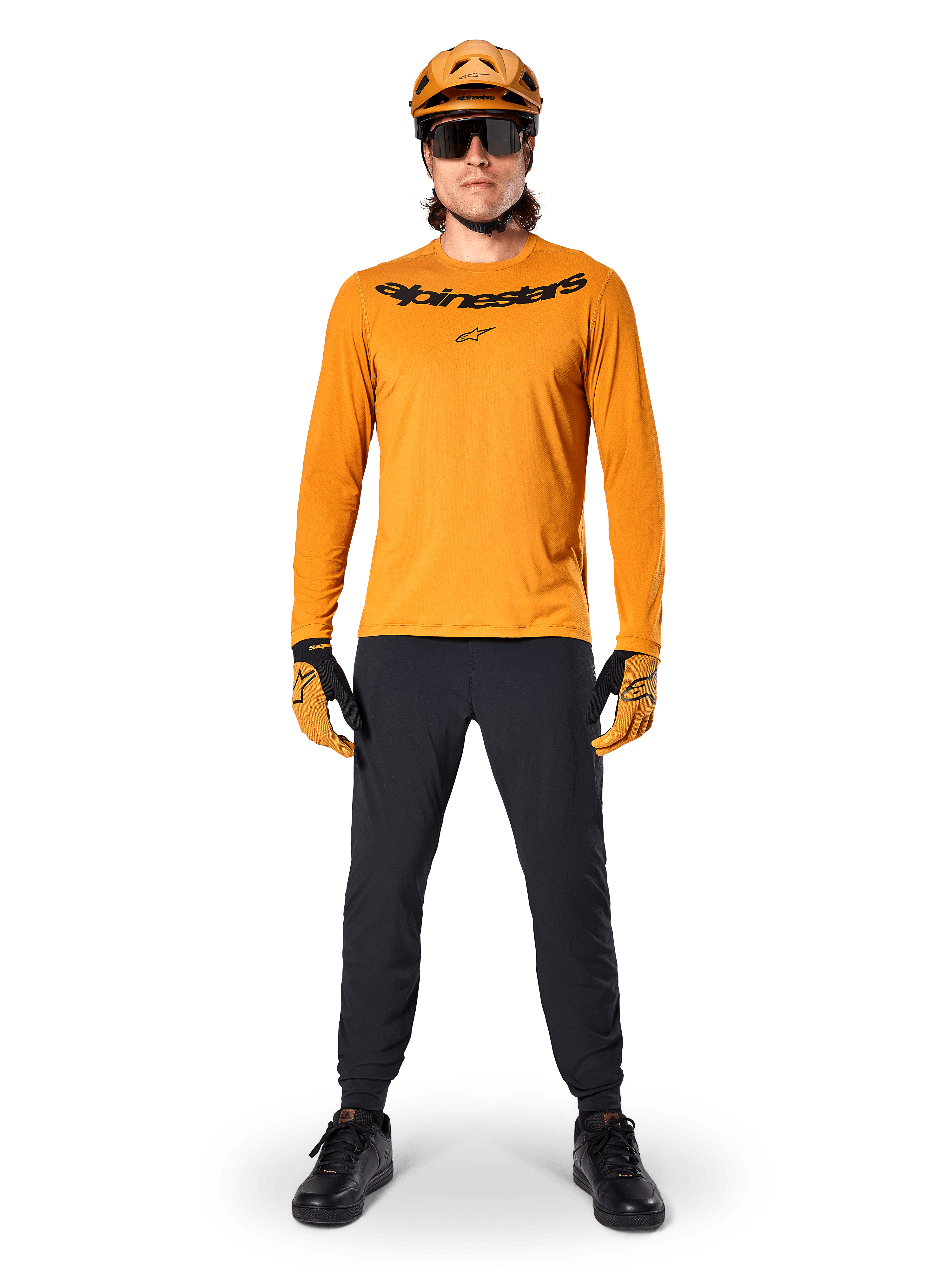 Koszulka z długim rękawem Alpinestars A-Dura Rocker w kolorze ciemnozłotym, z czarnym logo na piersi, w zestawie z dopasowanym złotym kaskiem MTB, czarnymi okularami przeciwsłonecznymi i czarnymi spodniami, profesjonalny strój do kolarstwa górskiego