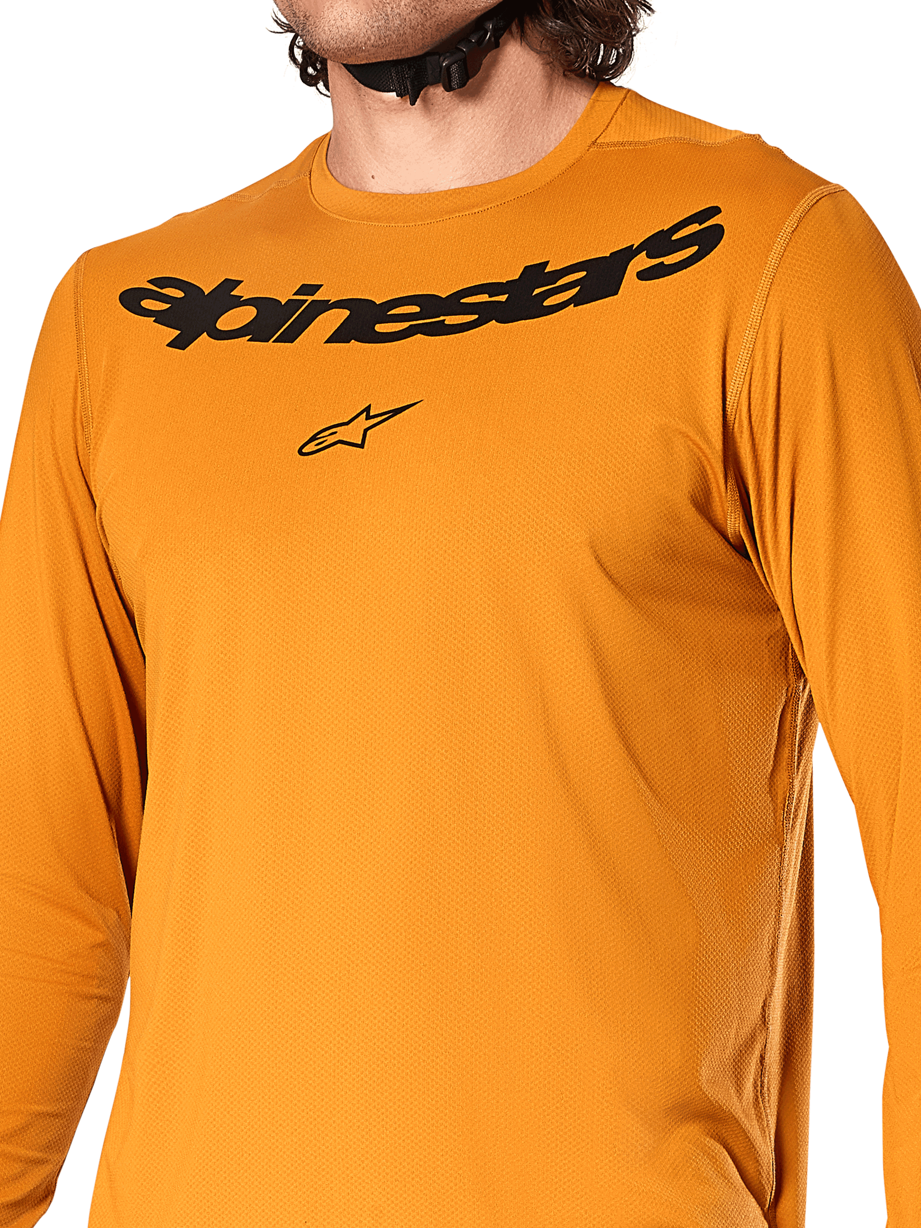 Alpinestars A-Dura Rocker Long Sleeve Jersey, kolor ciemnozłoty, zbliżenie na klatkę piersiową z czarnym napisem Alpinestars i logo gwiazdy, teksturowany dżakardowy materiał odprowadzający wilgoć, techniczna odzież rowerowa MTB