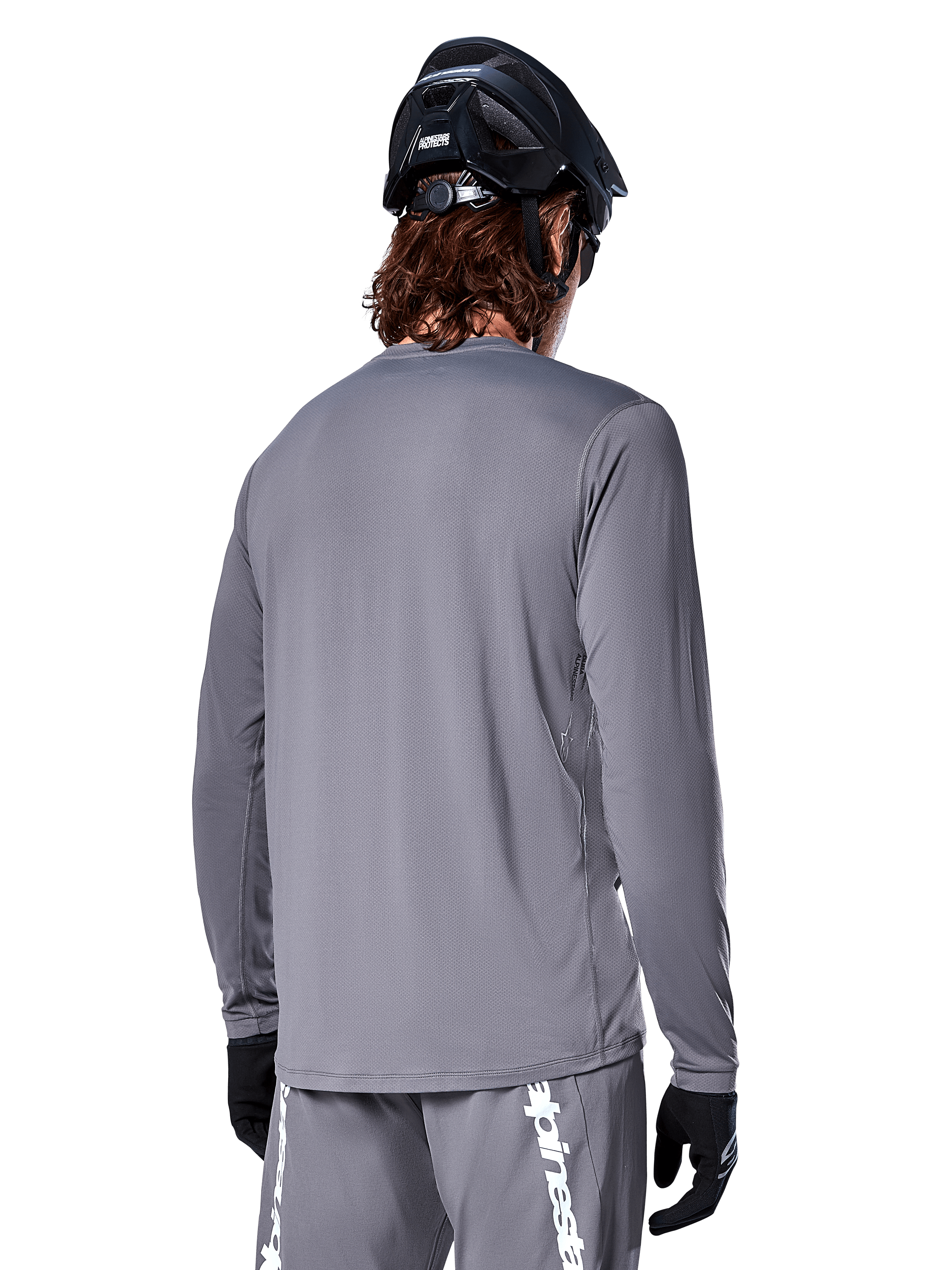 Alpinestars A-Dura Rocker Long Sleeve Jersey, ciemnoszara koszulka rowerowa z długim rękawem, widok kolarza górskiego od tyłu, pasujące szare spodenki z białym logo, czarny kask MTB i czarne rękawiczki, profesjonalna odzież do kolarstwa terenowego