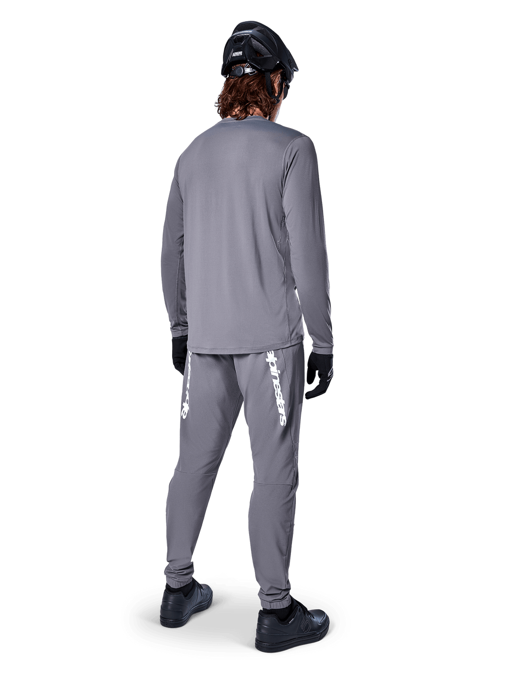 Koszulka Alpinestars A-Dura Rocker Long Sleeve, ciemnoszara, widok z tyłu modelu w pasujących szarych spodniach MTB, czarnym kasku i czarnych rękawiczkach, profesjonalny design odzieży do kolarstwa górskiego