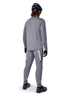 Koszulka Alpinestars A-Dura Rocker Long Sleeve, ciemnoszara, widok z tyłu modelu w pasujących szarych spodniach MTB, czarnym kasku i czarnych rękawiczkach, profesjonalny design odzieży do kolarstwa górskiego