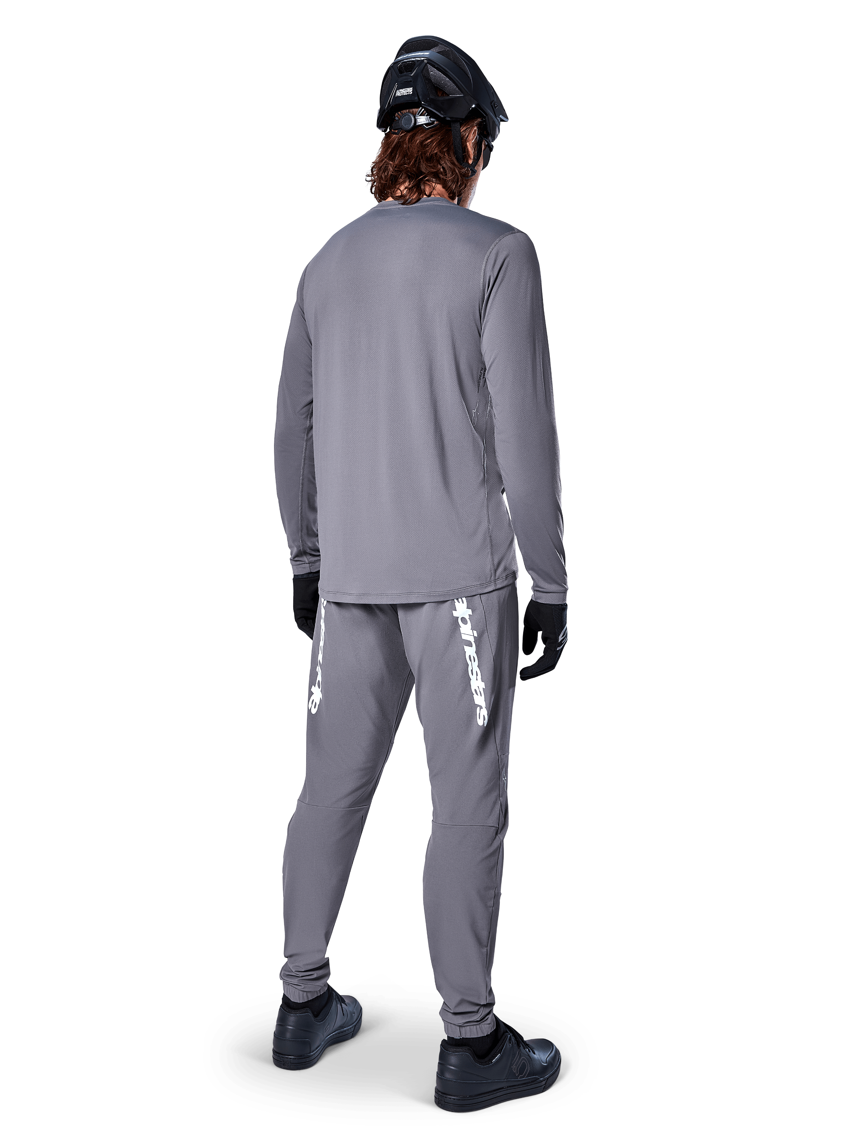 Koszulka Alpinestars A-Dura Rocker Long Sleeve, ciemnoszara, widok z tyłu modelu w pasujących szarych spodniach MTB, czarnym kasku i czarnych rękawiczkach, profesjonalny design odzieży do kolarstwa górskiego