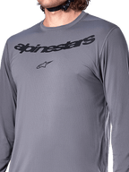 Alpinestars A-Dura Rocker Long Sleeve Jersey, ciemnoszary, zbliżenie na klatkę piersiową z czarnym napisem Alpinestars i logo gwiazdy, żakardowy materiał poliestrowo-spandexowy, wyczynowa odzież na rower górski