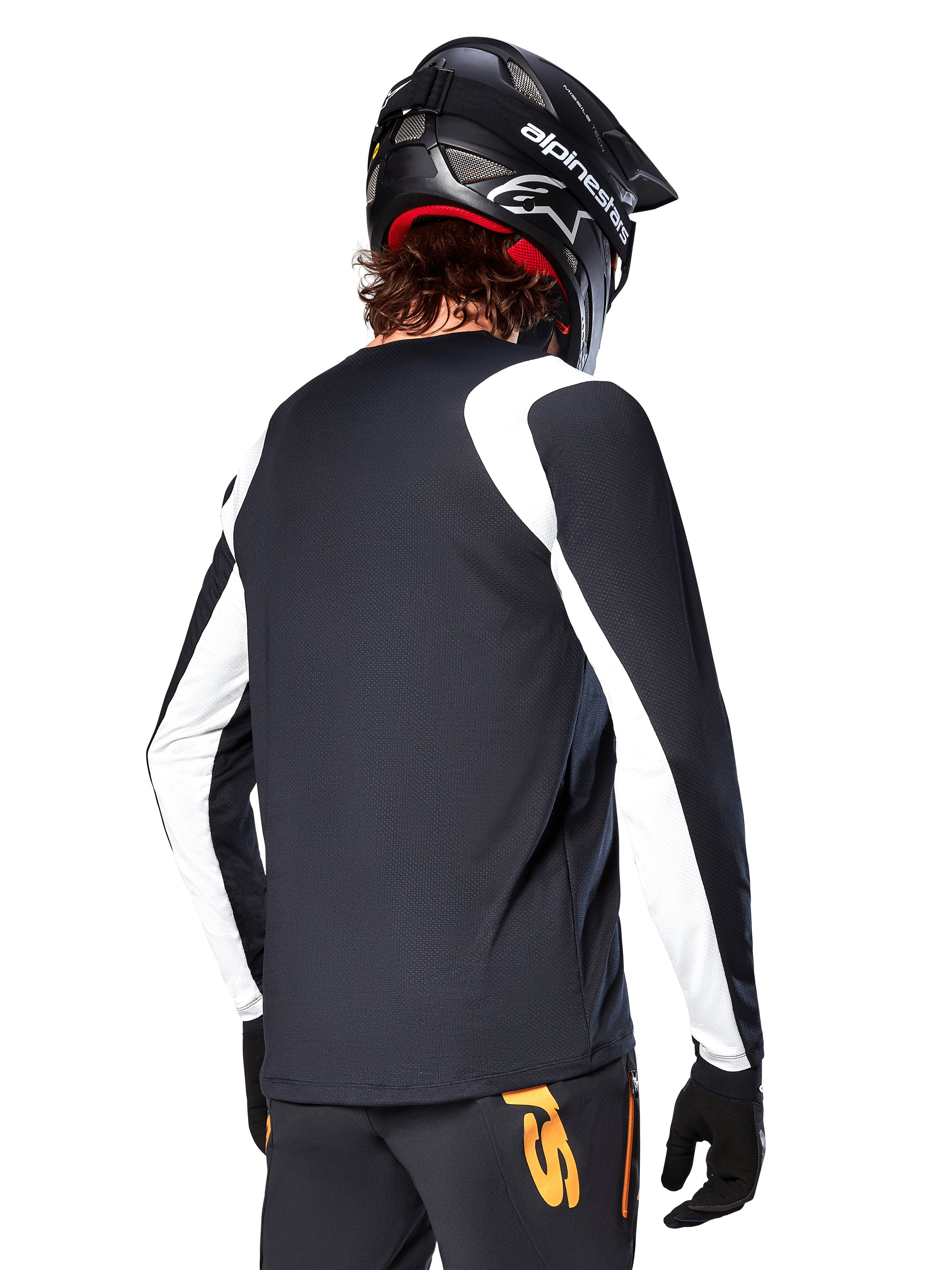 Rowerzysta MTB ubrany w koszulkę Alpinestars A-Supra Oscar z długim rękawem, czarna z białymi panelami na ramionach i rękawach, widok z tyłu, czarny kask i rękawice, spodnie z pomarańczowymi akcentami, wytrzymała odzież rowerowa off-road