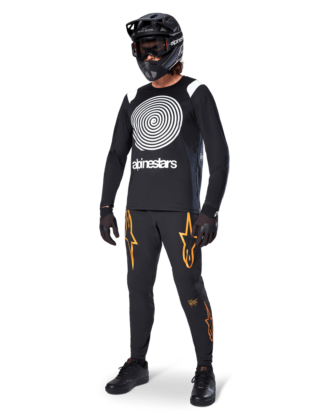 Rowerzysta MTB w koszulce Alpinestars A-Supra Oscar z długim rękawem w kolorze czarnym, z białą spiralną grafiką Oscar w stylu vintage, czarne spodnie z pomarańczowym logo gwiazdy, czarny kask typu full-face z goglami i czarne rękawice, profesjonalny sprzęt do kolarstwa górskiego