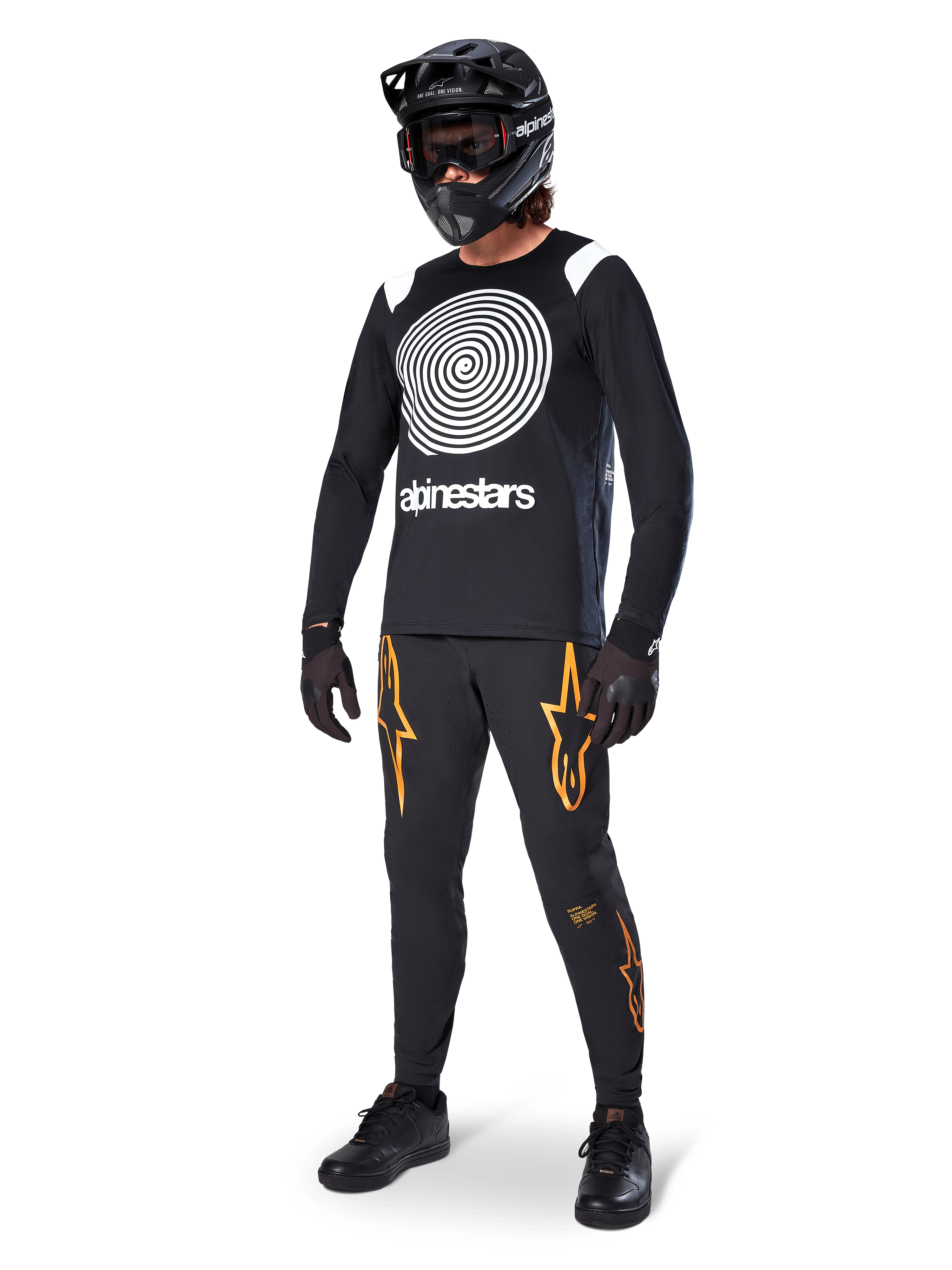 Rowerzysta MTB w koszulce Alpinestars A-Supra Oscar z długim rękawem w kolorze czarnym, z białą spiralną grafiką Oscar w stylu vintage, czarne spodnie z pomarańczowym logo gwiazdy, czarny kask typu full-face z goglami i czarne rękawice, profesjonalny sprzęt do kolarstwa górskiego