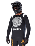 Alpinestars A-Supra Oscar Long Sleeve Jersey, koszulka rowerowa MTB, czarno-biała, z wyrazistym białym spiralnym wzorem i logo Alpinestars na klatce piersiowej, noszona z czarnym kaskiem full-face i goglami, profesjonalna odzież do kolarstwa górskiego