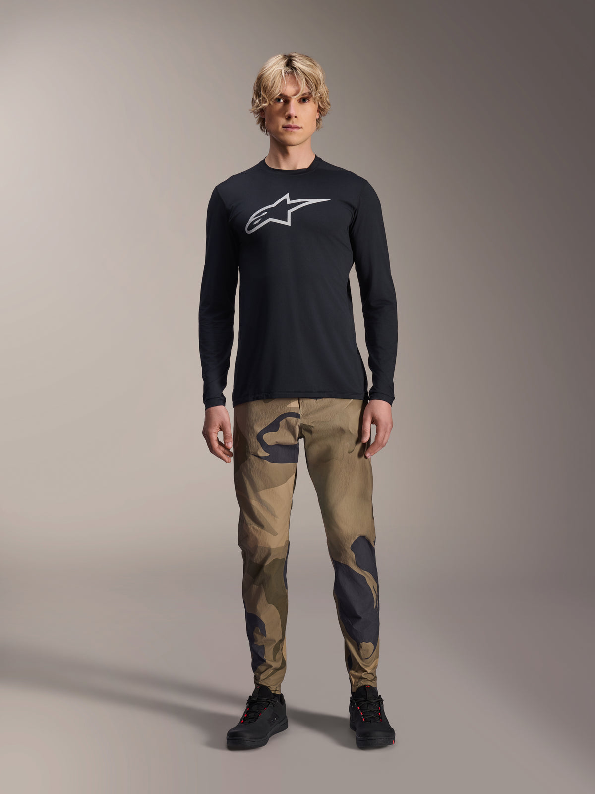 Alpinestars A-Dura Camo Pant, MTB Cycling Pants, Brown and Green Camouflage, worn with a black long-sleeve jersey and black shoes, sporty mountain bike style with durable stretch fabric