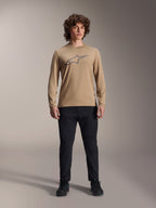 Alpinestars A-Dura Astar Long Sleeve Jersey, jasnobrązowa koszulka z długim rękawem z szarym logo Astars na piersi, noszona przez modela w czarnych spodniach technicznych i butach, casualowa odzież wyczynowa MTB