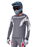 Alpinestars A-Supra Race Jersey - Long Sleeve, ciemnoszara koszulka z długim rękawem, białe i czerwone akcenty, grafika w stylu wyścigowym, noszona z pasującymi szarymi spodniami, niebieskim kaskiem full-face i białymi rękawicami, profesjonalny sprzęt do MTB i downhillu