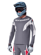 Alpinestars A-Supra Race Jersey - Long Sleeve, ciemnoszara koszulka z długim rękawem, białe i czerwone akcenty, grafika w stylu wyścigowym, noszona z pasującymi szarymi spodniami, niebieskim kaskiem full-face i białymi rękawicami, profesjonalny sprzęt do MTB i downhillu
