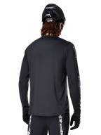 Alpinestars A-Dura Switch Long Sleeve Jersey, Black, rear view on a cyclist wearing a black MTB helmet and gloves, featuring technical jacquard fabric and a drop tail for off-road riding