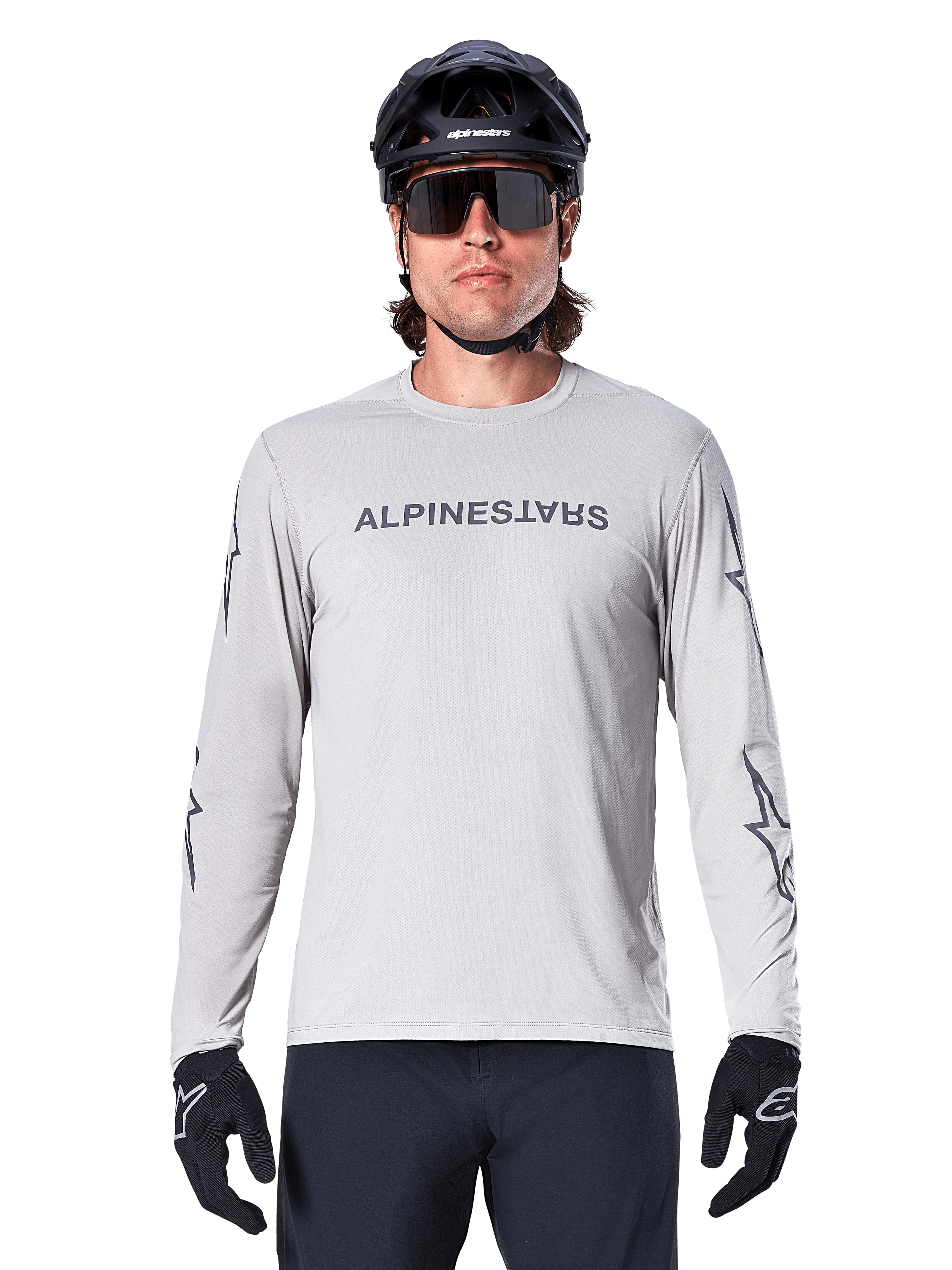 Alpinestars A-Dura Switch Long Sleeve Jersey, jasnoszara, posiada ciemnoszary napis na klatce piersiowej i logotypy gwiazdy na rękawach, noszona przez rowerzystę w czarnym kasku MTB i rękawiczkach, wydajna odzież rowerowa do jazdy po szlakach