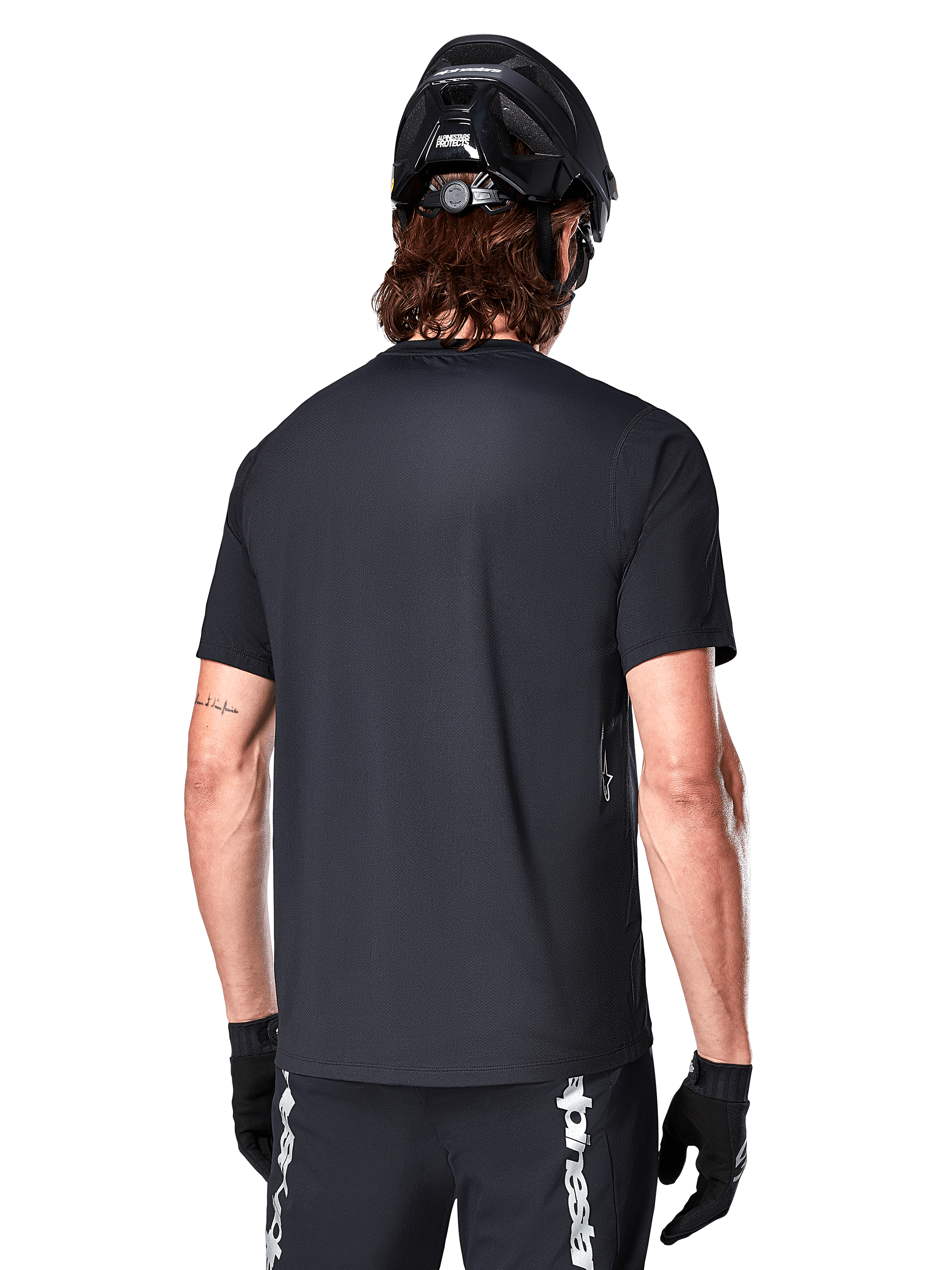 Alpinestars A-Dura Switch Short Sleeve Jersey, czarna, widok z tyłu na modelu w czarnym kasku rowerowym i spodenkach MTB, podkreślający regularny krój i przedłużony tył do jazdy na rowerze górskim